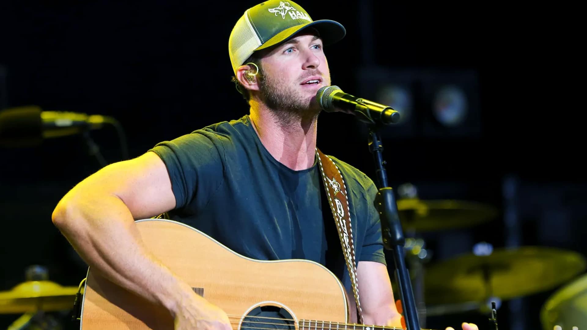 Riley Green performs on stage with his guitar and cap, recalling how he nearly turned down a Birmingham venue where Chris Stapleton once struggled to sell tickets but later sold it out himself.