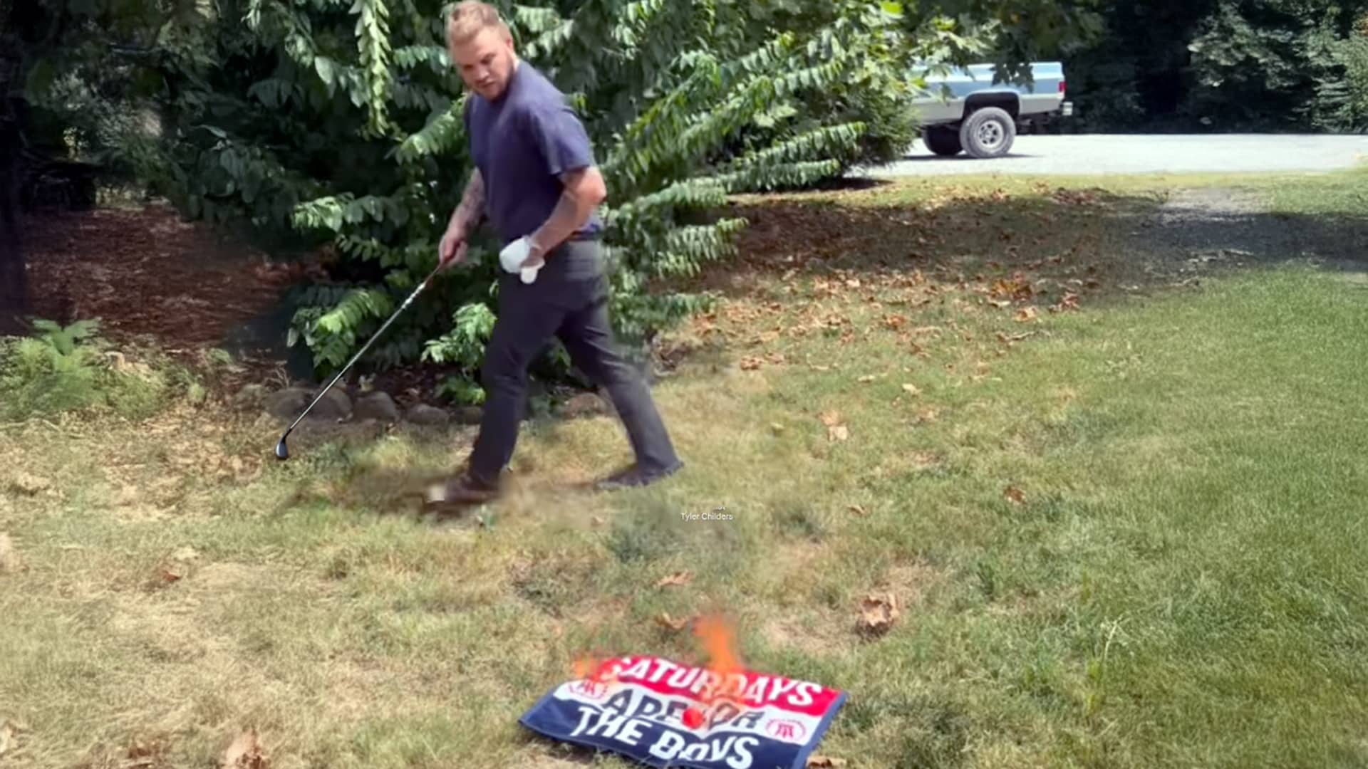 Zach Bryan stands with a golf club beside a burning Barstool Sports flag as Tyler Childers’ song plays during a heated breakup moment.