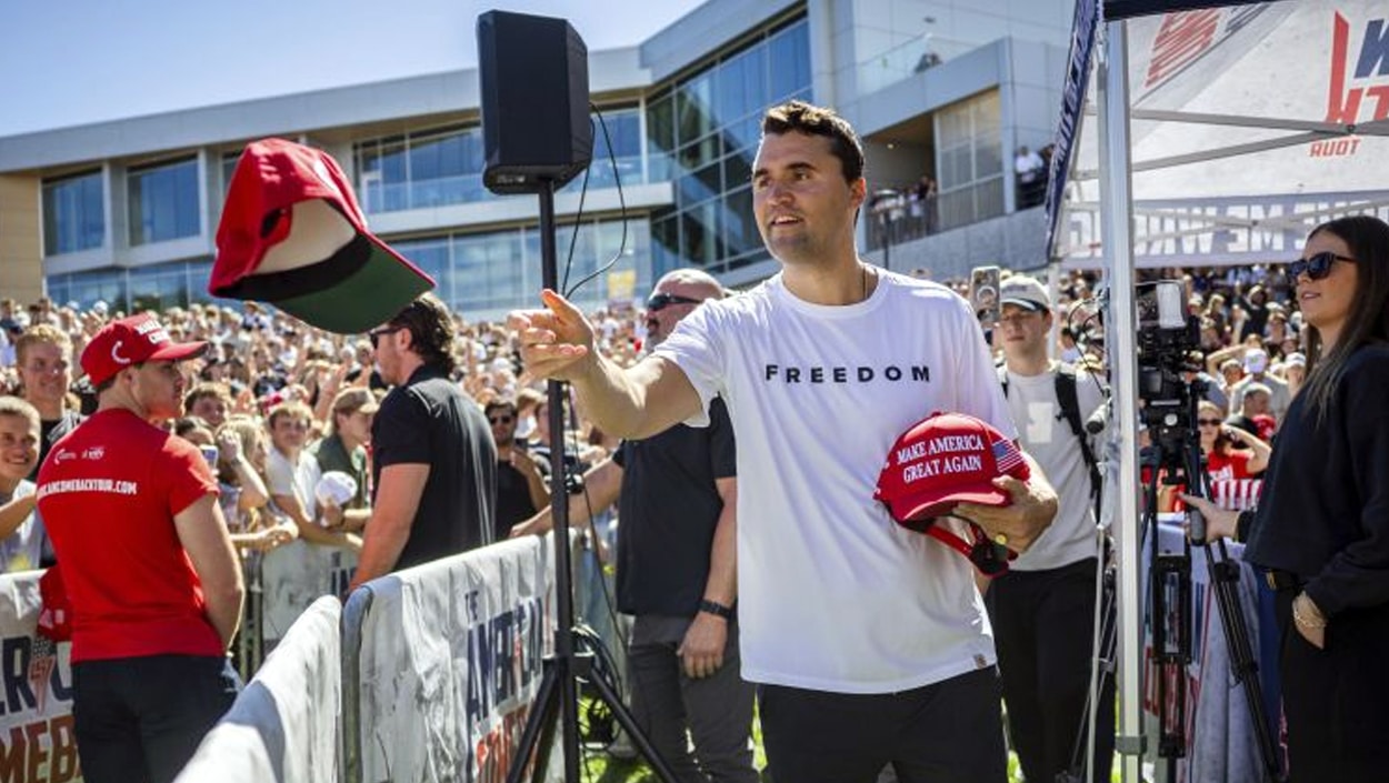Charlie Kirk at a Utah campus event in a white “FREEDOM” shirt, handing out MAGA hats before the fatal shooting.