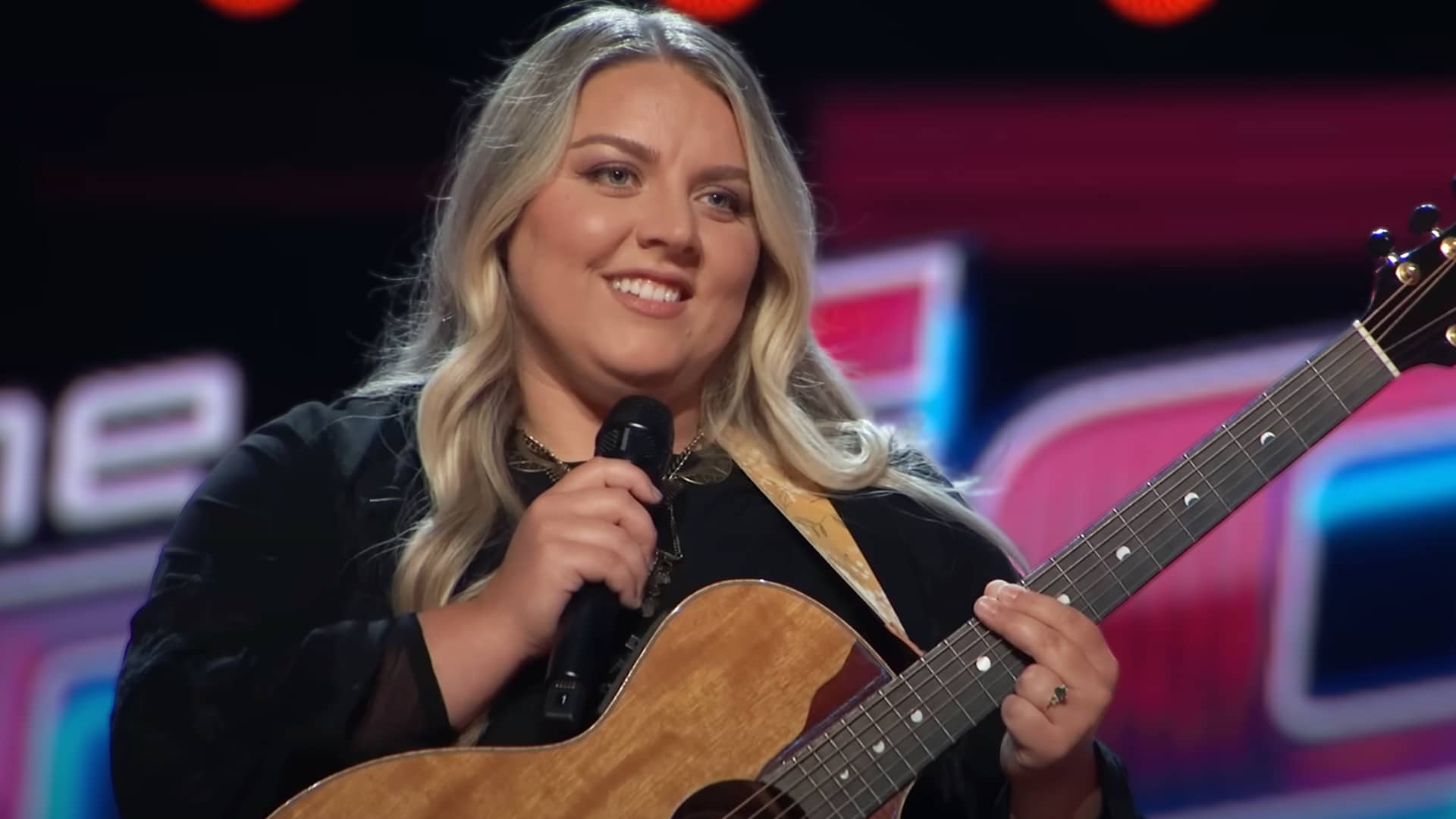 Contestant Cori Kennedy holds her guitar on The Voice, impressing coaches with both a Judds classic and her own original song.