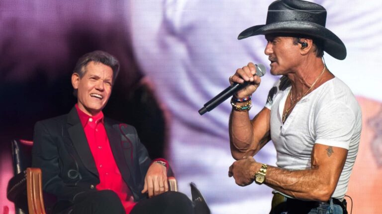 Tim McGraw sings into a microphone while Randy Travis smiles beside him during their surprise duet of “On the Other Hand.”