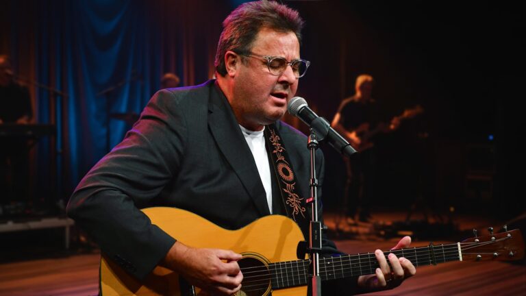 Vince Gill performing with his guitar onstage as he releases a powerful new extended version of “Go Rest High on That Mountain” 30 years later.