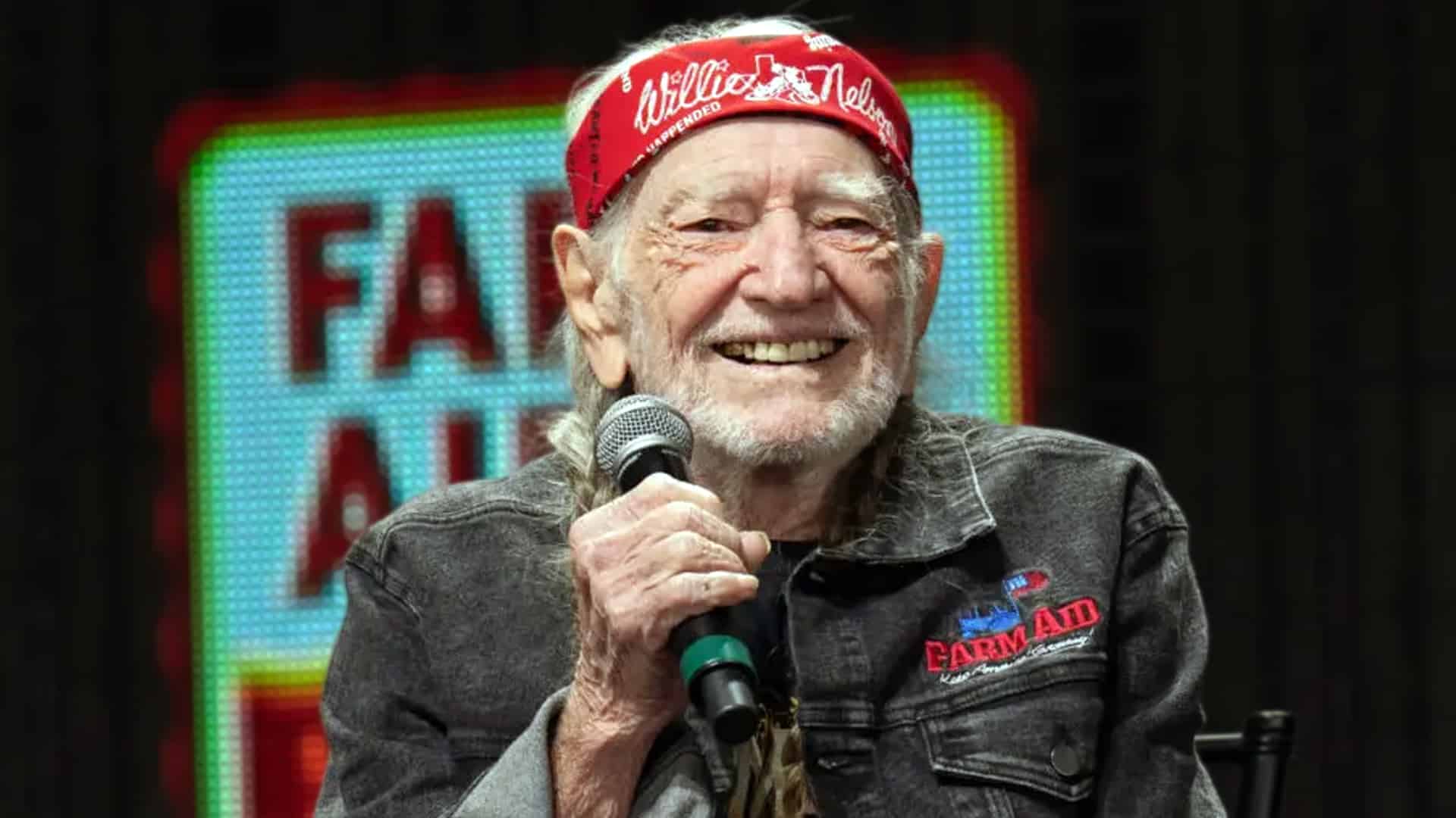 Willie Nelson smiling with a mic at Farm Aid, as Zac Brown recalls the country legend’s hilarious pre-show ritual with young artists.