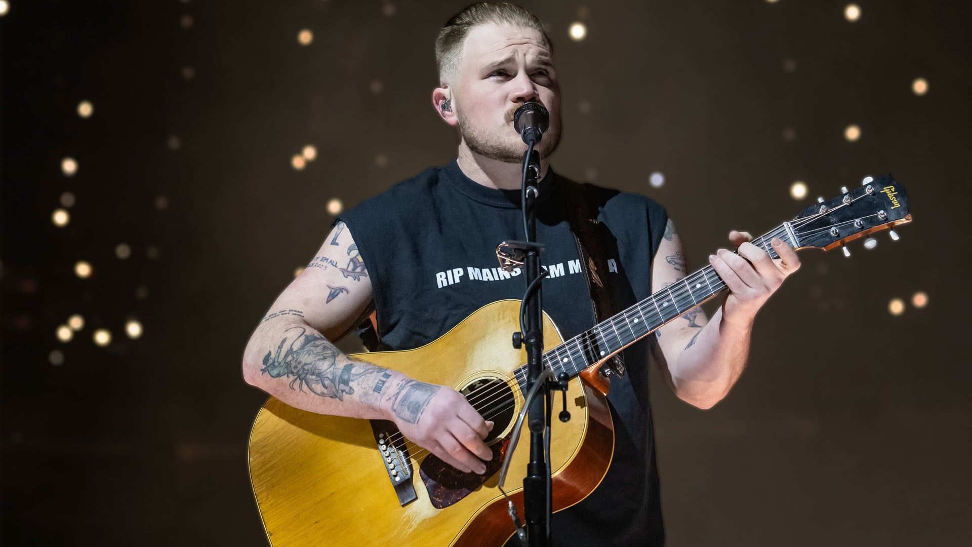 Zach Bryan performing with guitar in hand after breaking George Strait’s U.S. concert attendance record at Michigan Stadium.