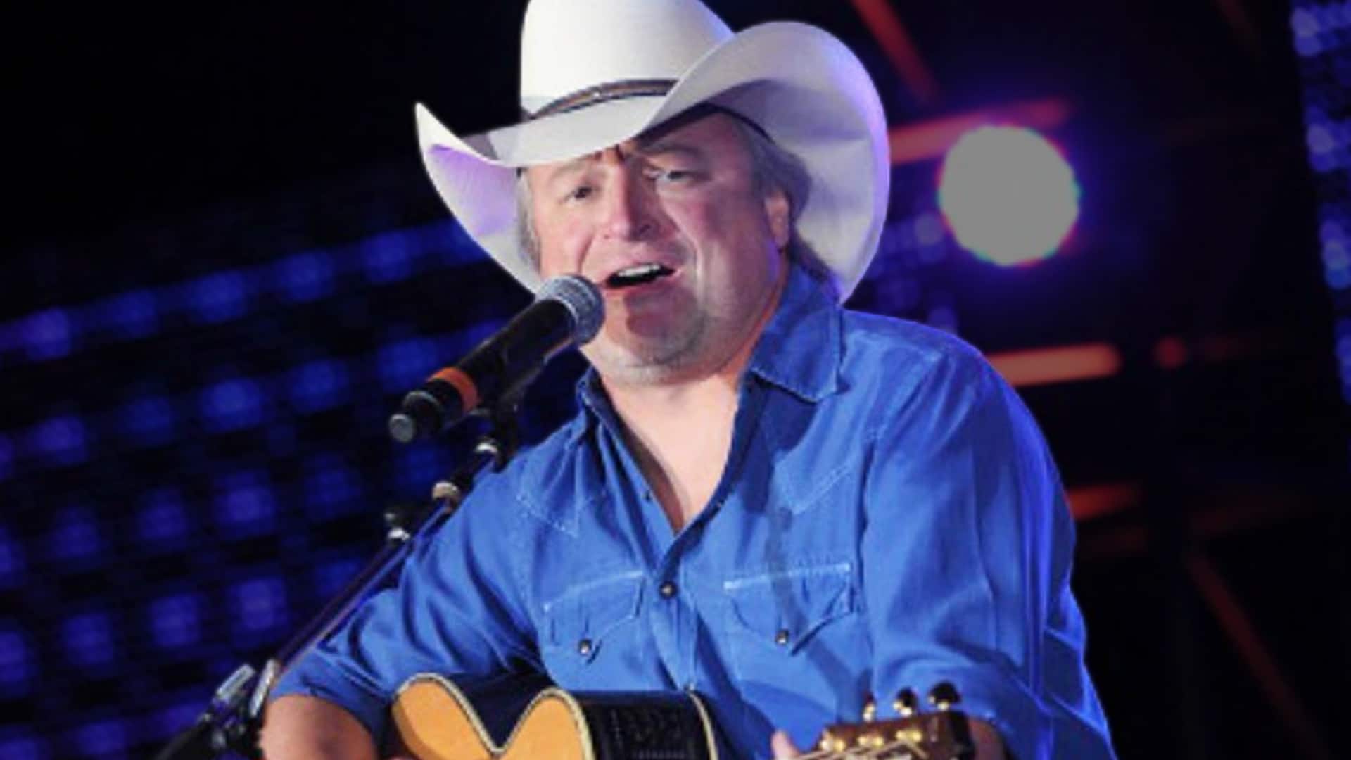 Country legend Mark Chesnutt plays guitar under stage lights, a reminder of his enduring '90s legacy amid new health concerns in Baton Rouge.