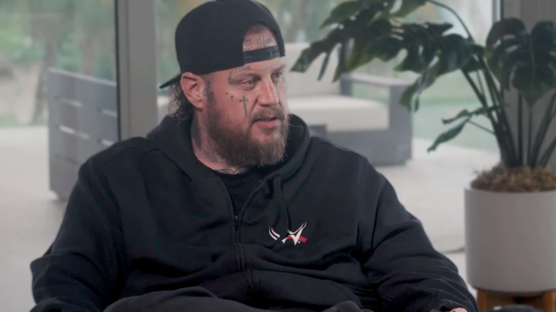 Country artist Jelly Roll in a black hoodie and cap, opening up about infidelity and redemption in an emotional conversation about love and growth.