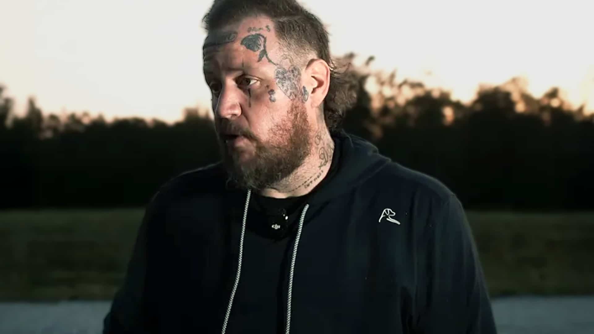 Jelly Roll standing outdoors at sunset, speaking passionately about his plan to build a free 100-acre rehab and mental health center in Tennessee.