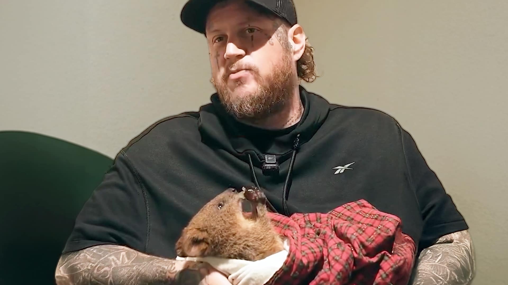 Jelly Roll holding a baby quokka wrapped in a plaid blanket, smiling softly during his Australia trip where he named the animal after Loretta Lynn.