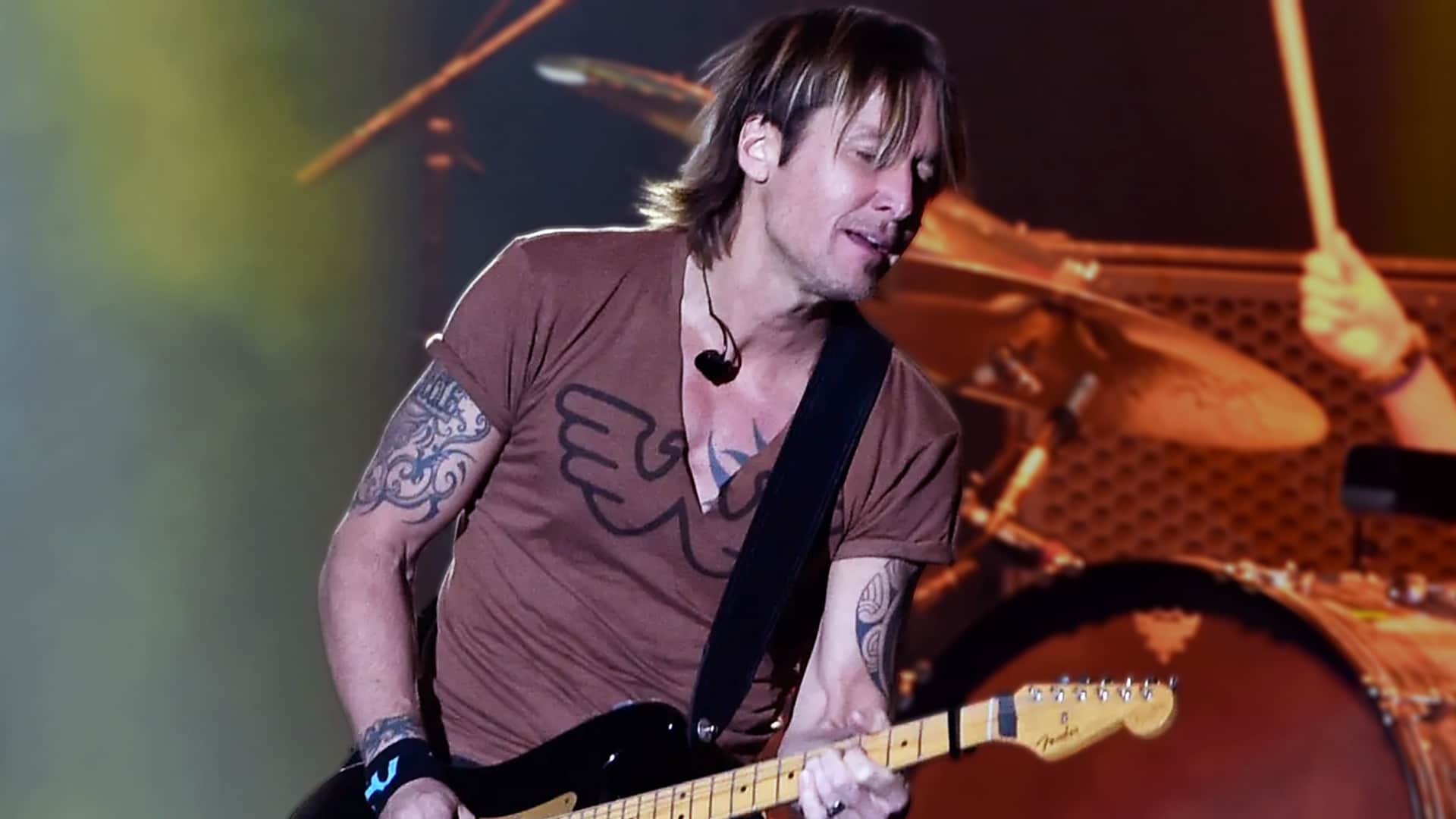 Keith Urban performing with his guitar under warm stage lights, before canceling his Greenville concert due to laryngitis.