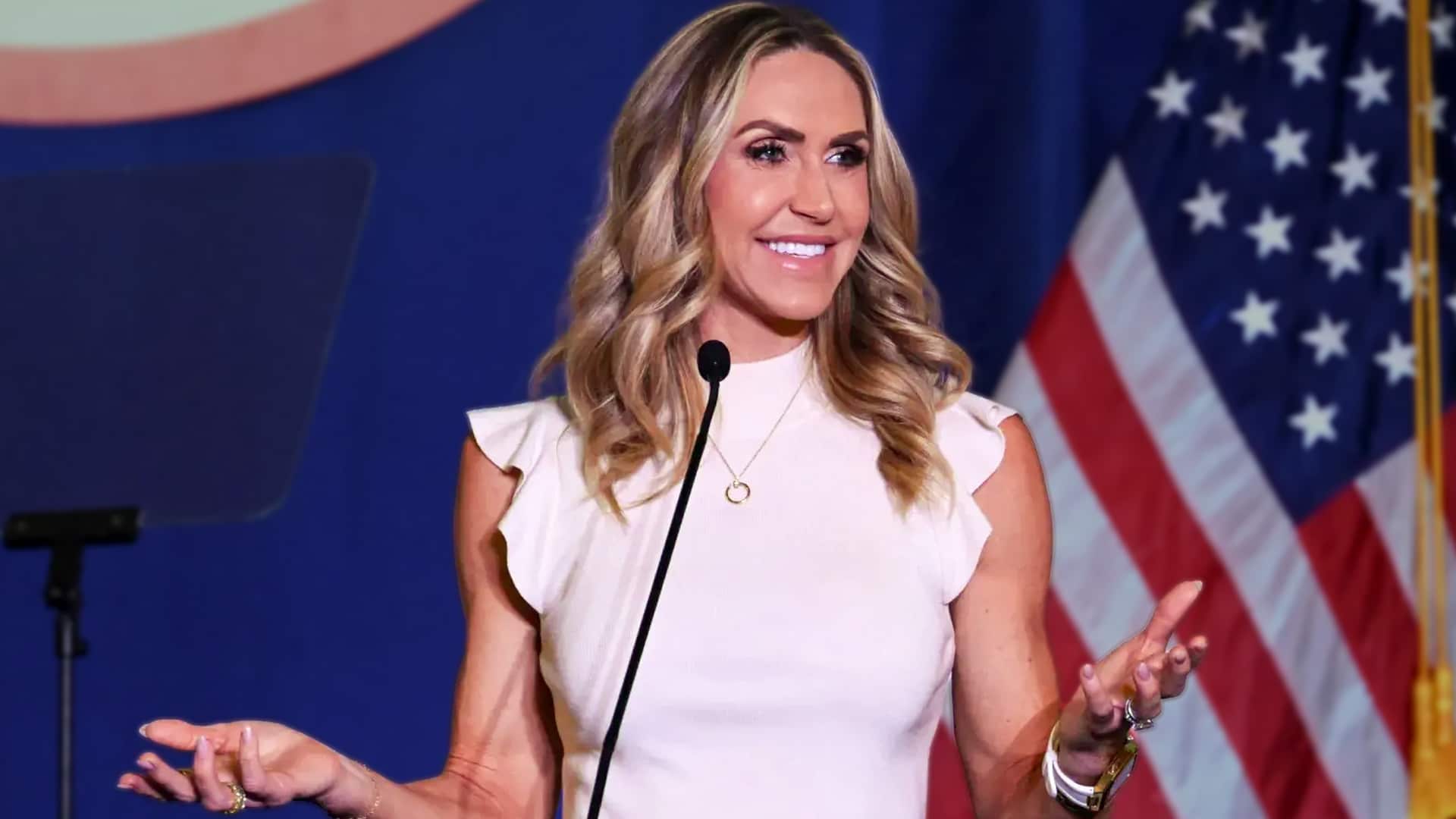 Lara Trump gestures mid-speech at a podium, blending politics and pop culture while volunteering to sing at Turning Point USA’s Super Bowl alternative show.