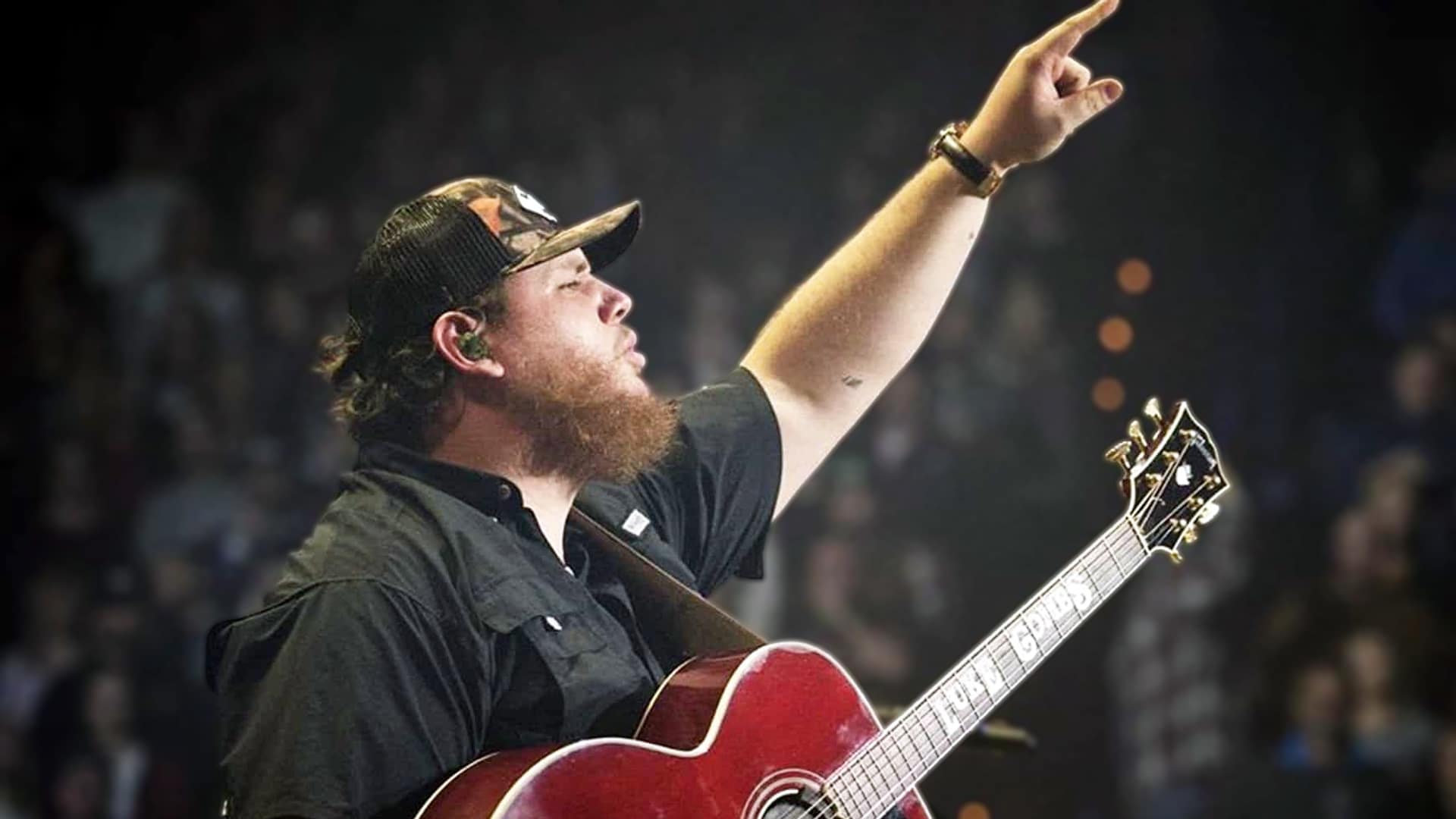 Luke Combs performing with his guitar onstage, raising his hand triumphantly after breaking Garth Brooks’ record as the highest-selling country artist ever.