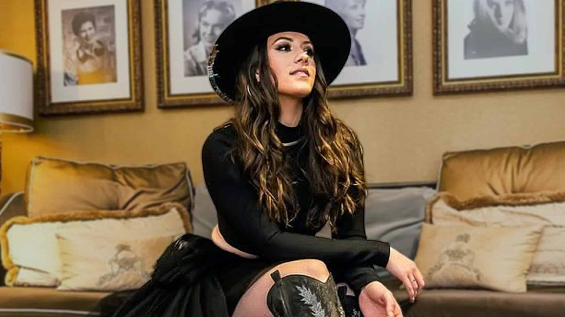 Maggie Baugh sitting confidently in a stylish black outfit, announcing her new single The Devil Win amid swirling Keith Urban rumors.