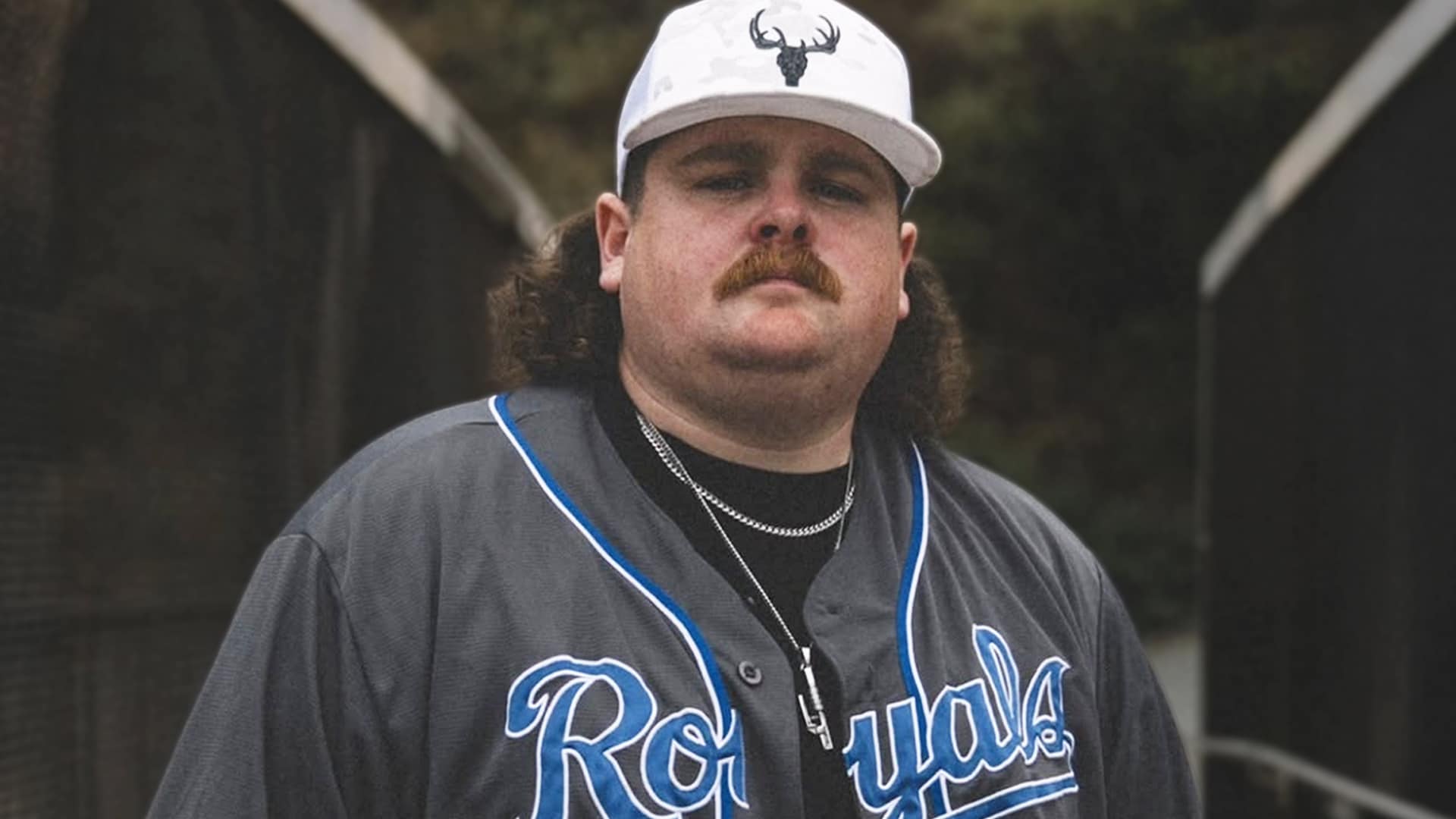 Rising artist Bryan Andrews, known for his unapologetically anti-MAGA stance, standing in a Royals jersey as his raw, working-class country message goes viral.