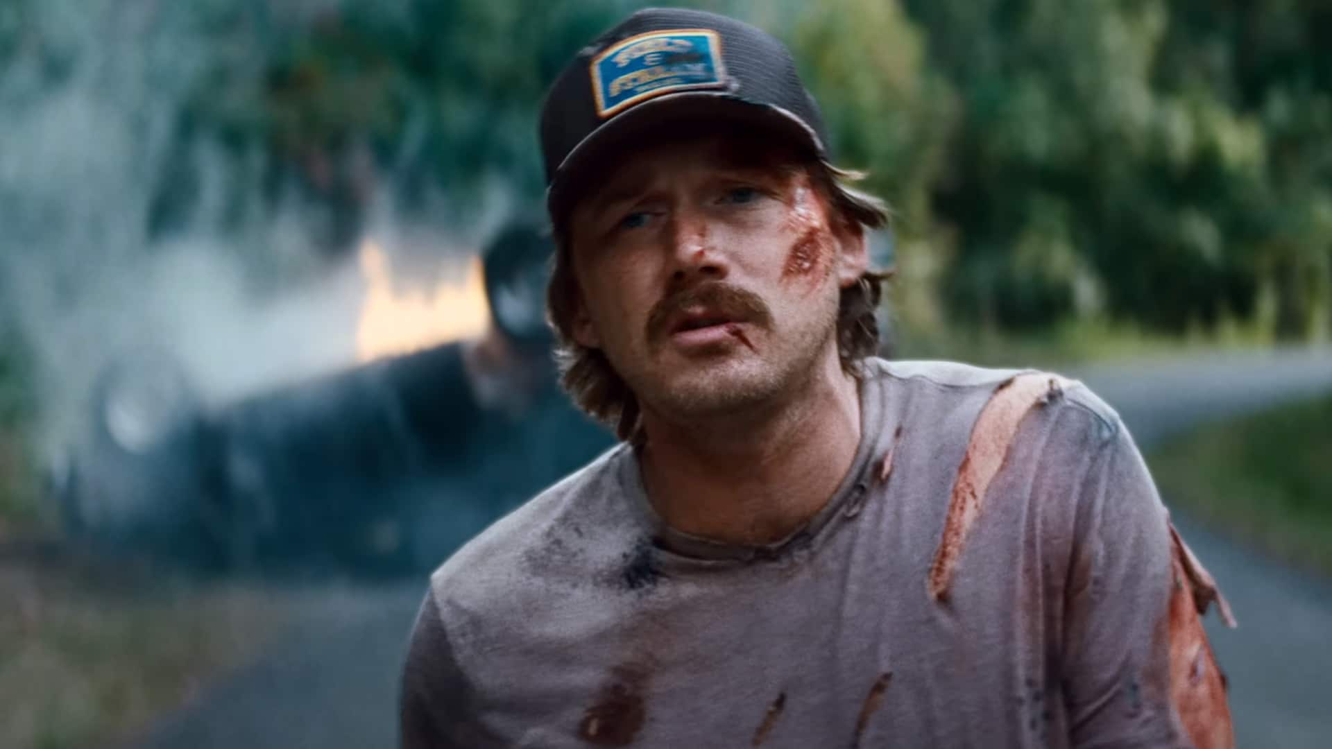 Morgan Wallen bloodied and bruised in the I Got Better video, walking away from a fiery crash as a breakup metaphor.