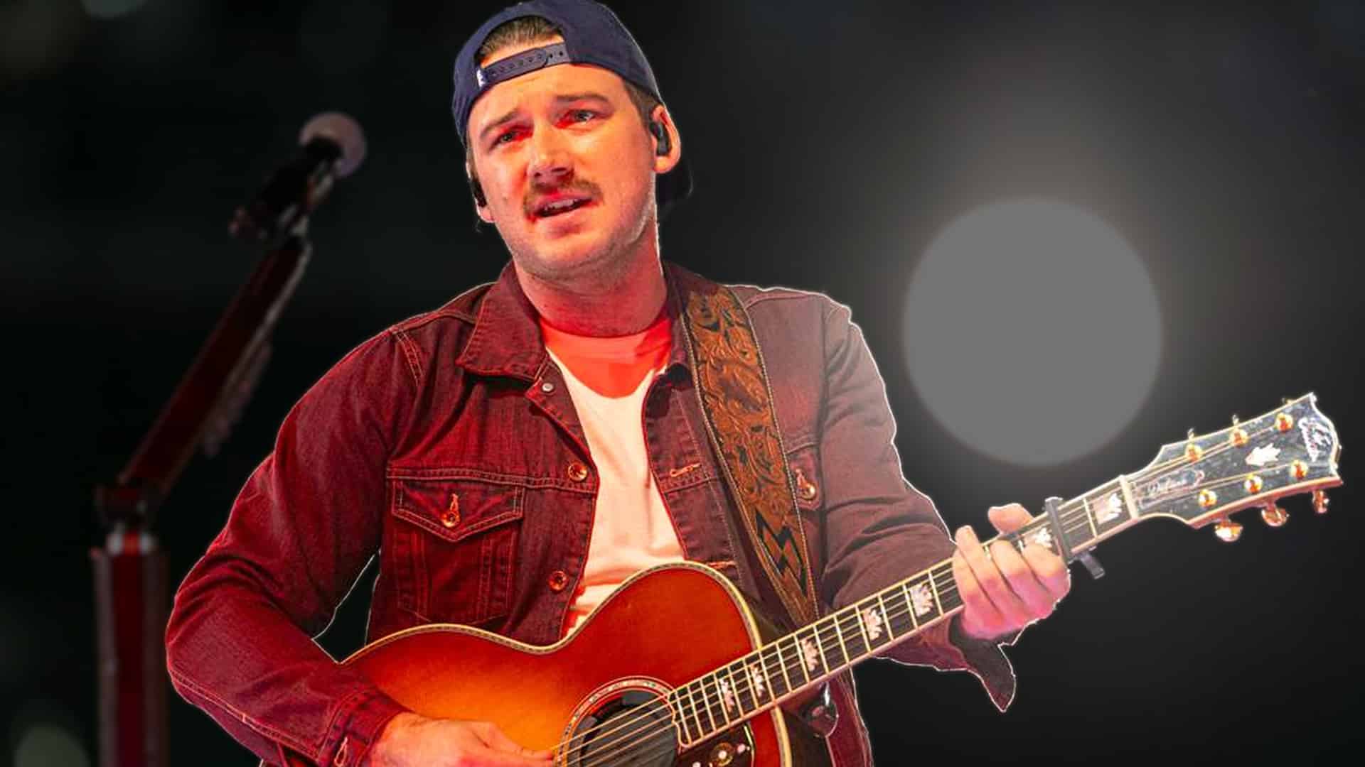 Morgan Wallen performing with an acoustic guitar under bright stage lights, showing the heartfelt side of the singer who recently surprised a fan with a prayer call.