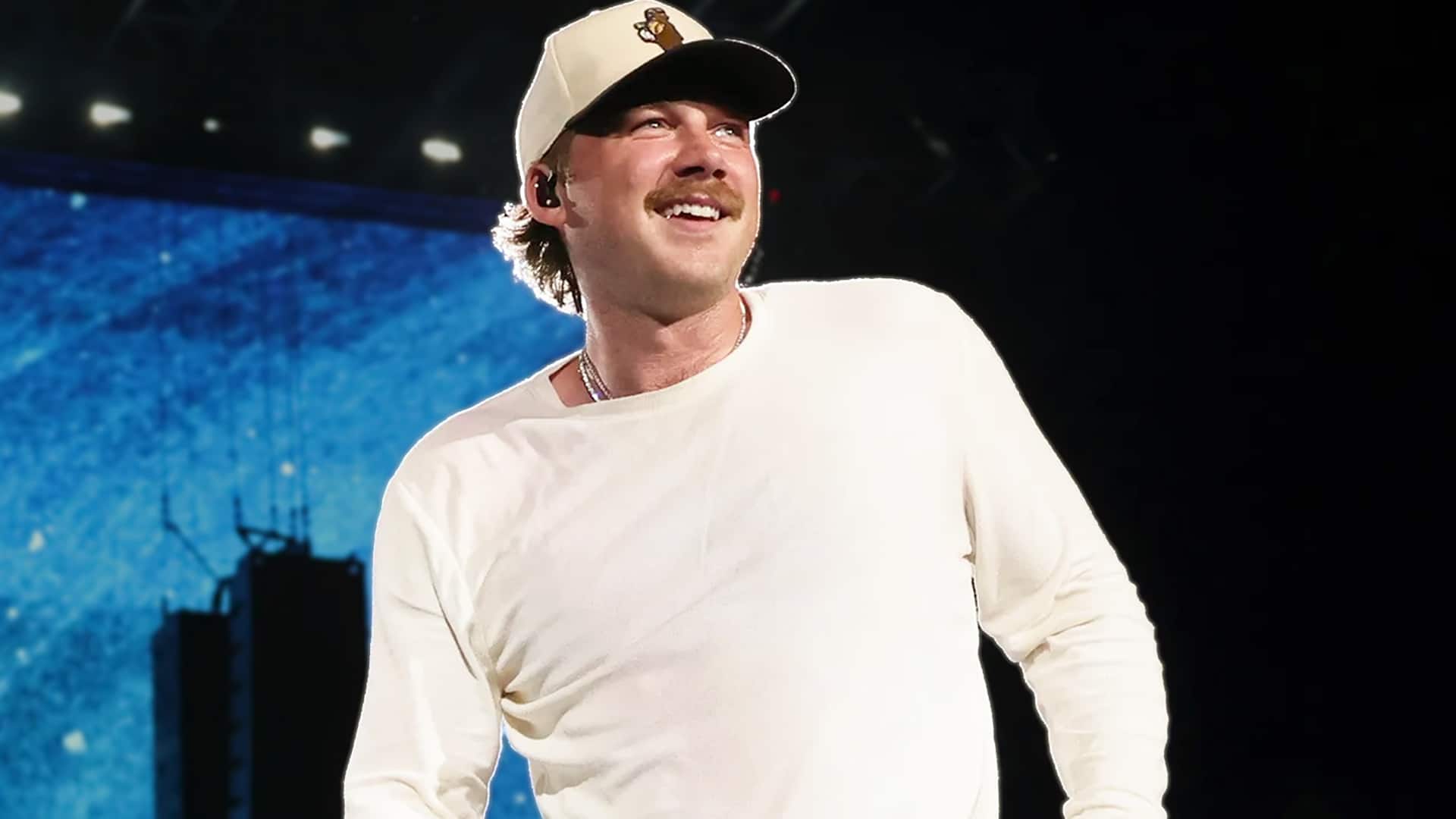 Morgan Wallen performing onstage in a white shirt and cap, appearing confident amid renewed headlines about his past arrest and comments about fellow artist Chris Young.
