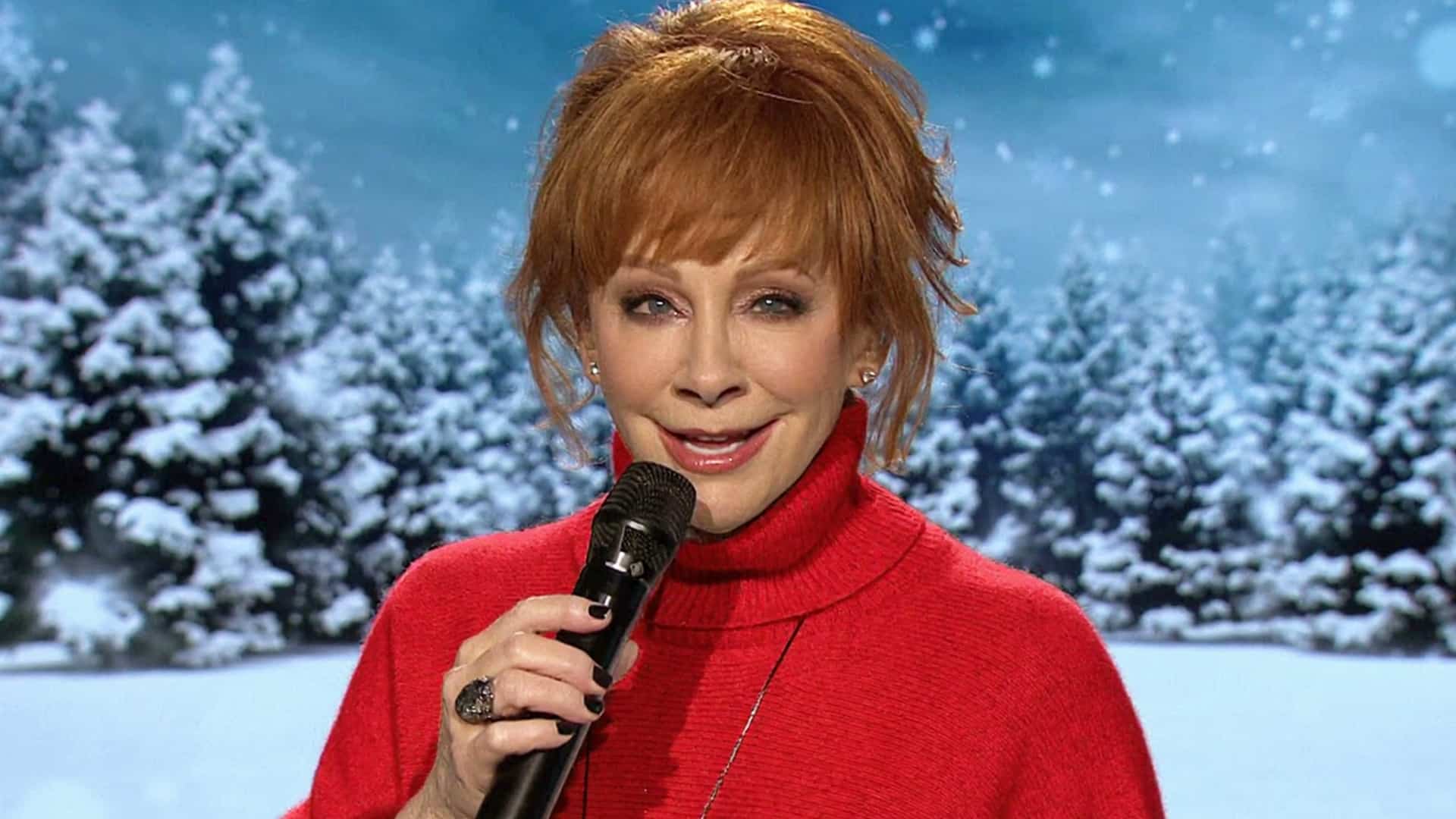 Reba McEntire, smiling with a microphone against a snowy backdrop, is ready to host and perform at this year’s Christmas in Rockefeller Center.