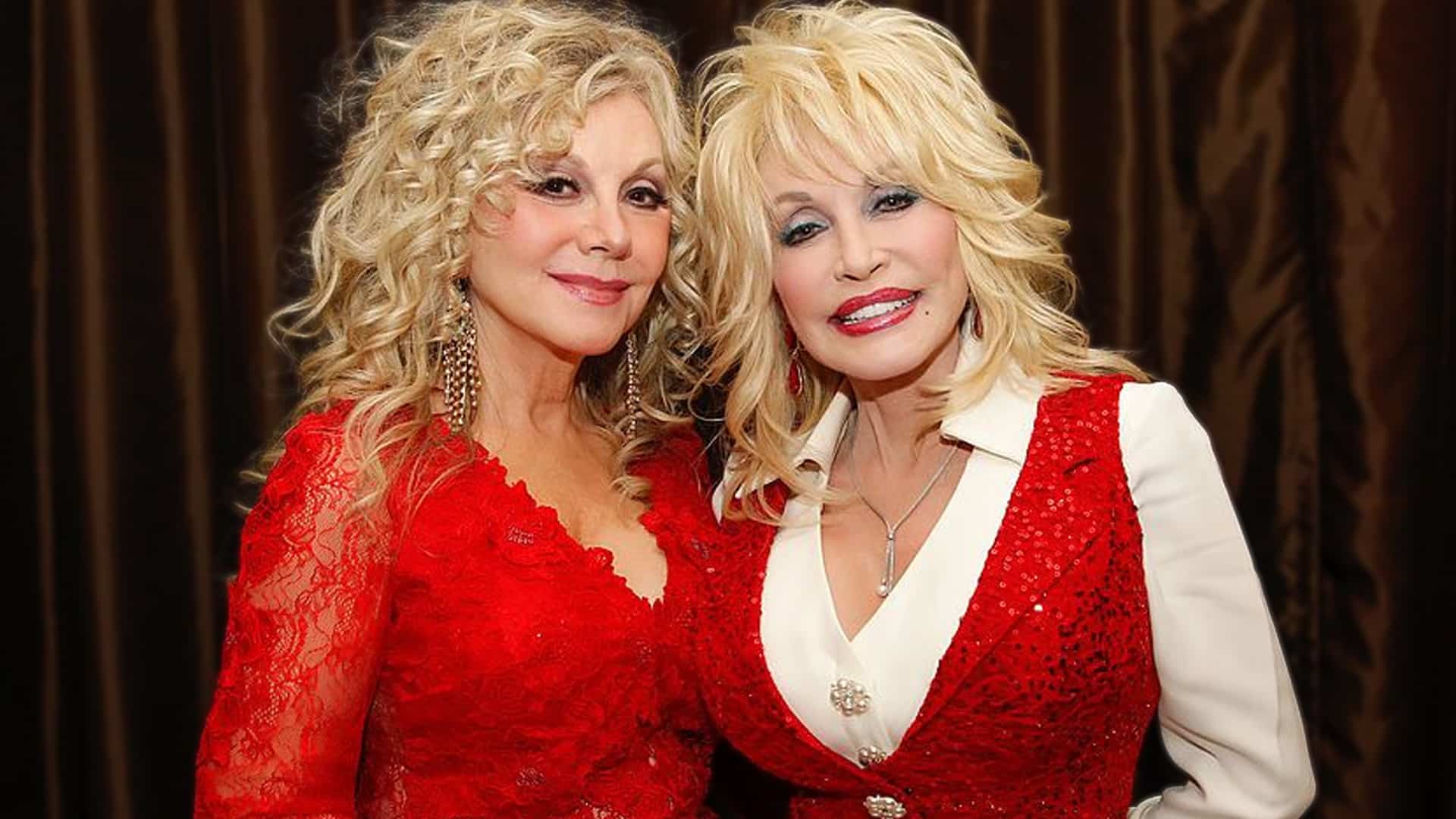 Stella Parton and Dolly Parton standing together in matching red outfits, united as Stella defends their sister Freida amid public concern over Dolly’s health.