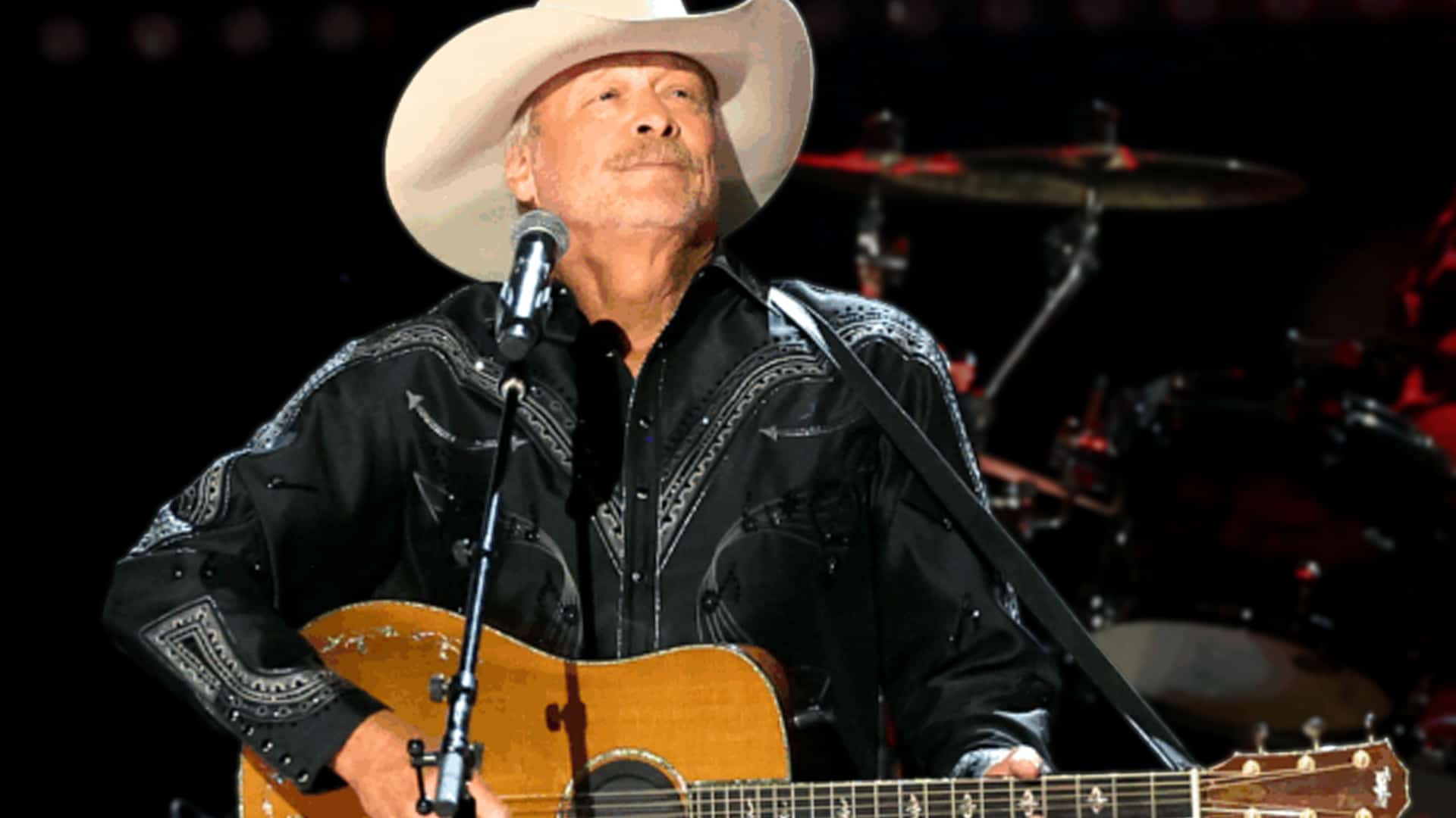 Alan Jackson performing onstage in a black embroidered shirt and cowboy hat, sharing the heartfelt reason behind his retirement from touring.