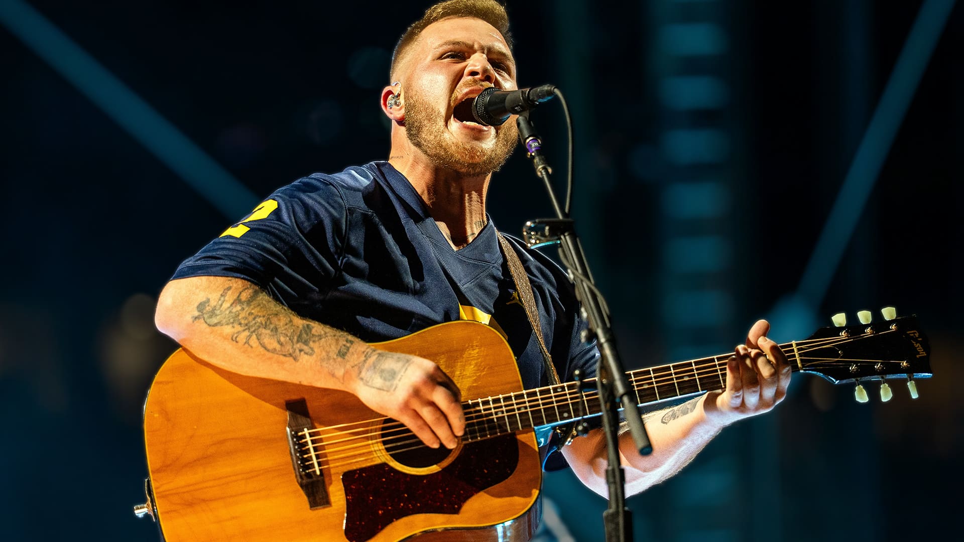 Country artist Zach Bryan singing onstage with intensity, reflecting the bold spirit of his track “Bad News” that challenges law enforcement and sparks debate.