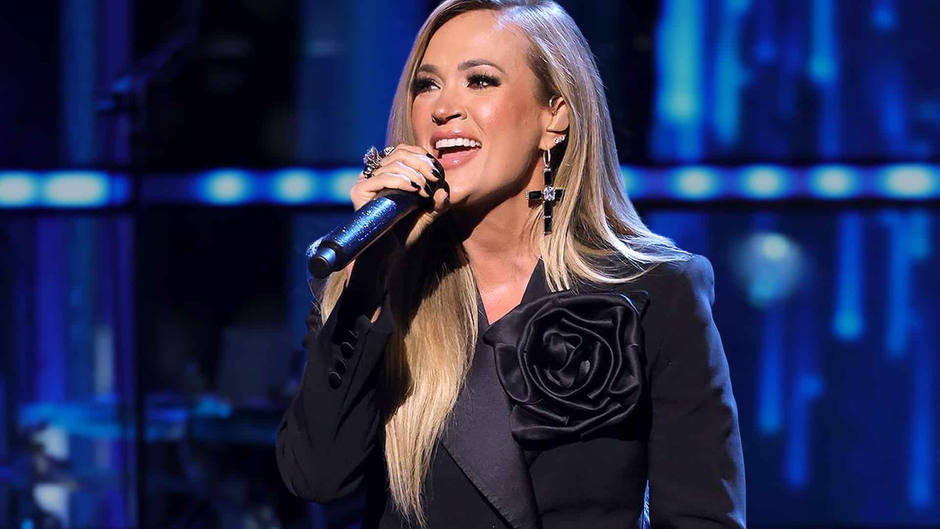 Country singer Carrie Underwood sings passionately into a microphone during a live performance, celebrating her achievement as the highest RIAA certified female country artist ever.