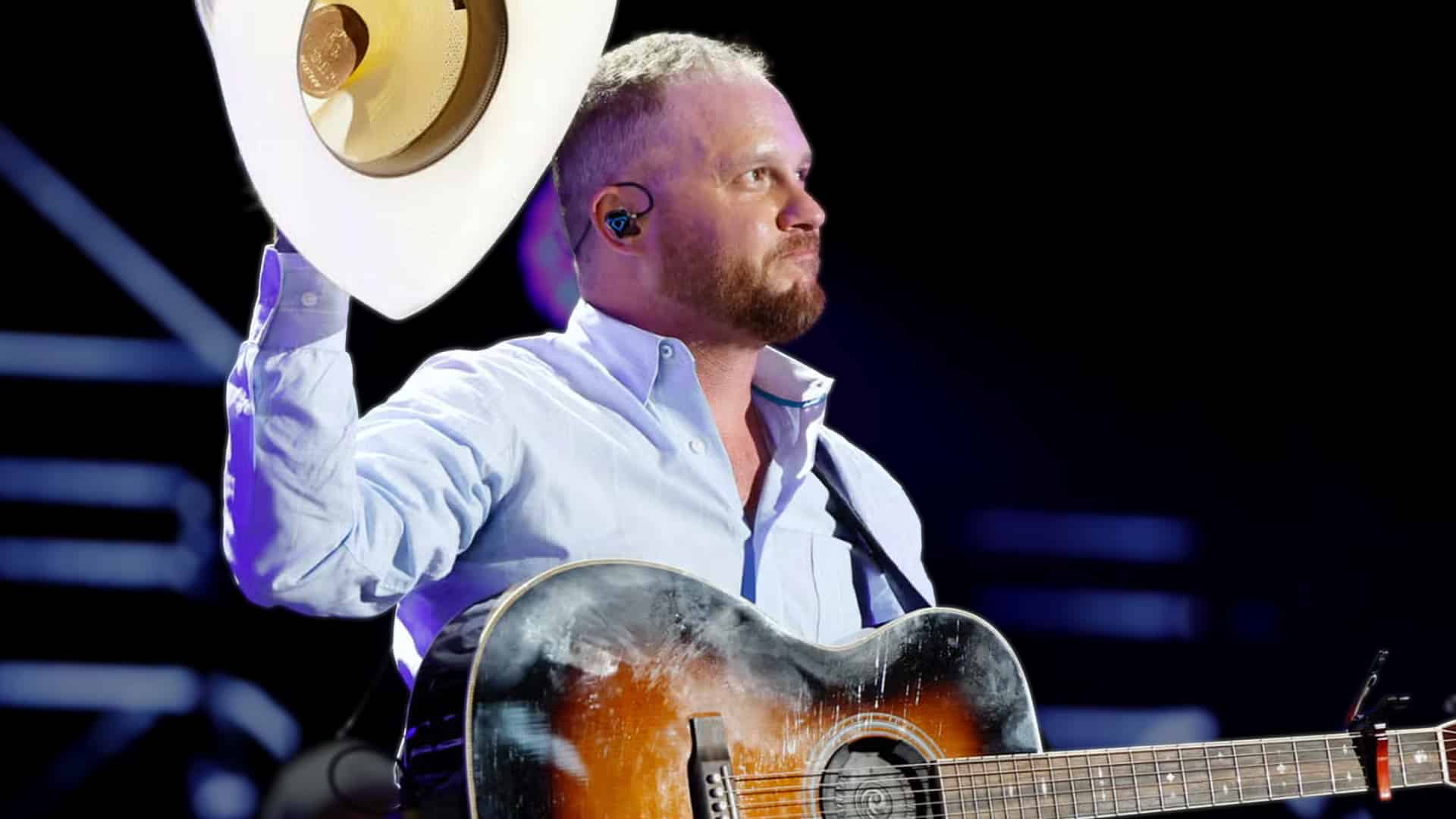 Cody Johnson raising his hat with a worn guitar across his chest, matching the mix of pride and frustration behind his decision to skip the 2025 CMA stage.