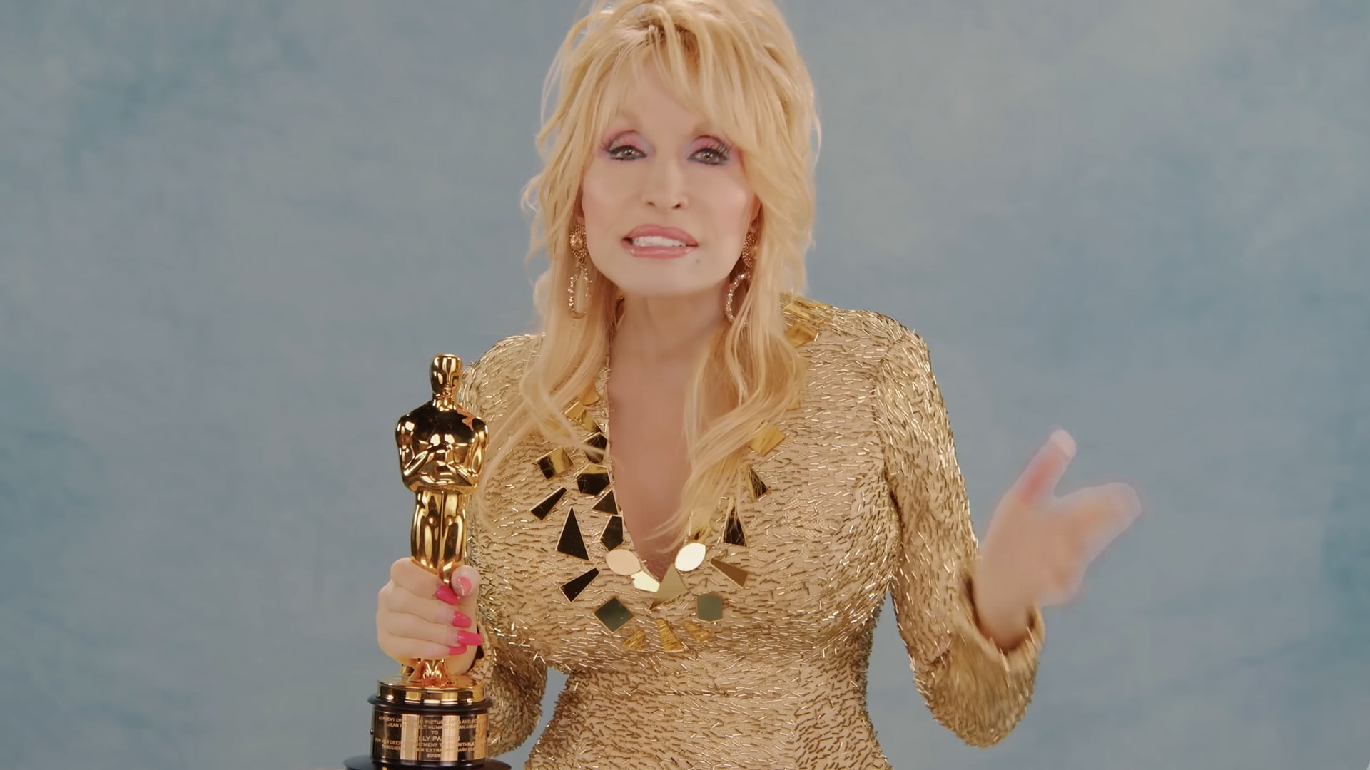 Dolly Parton in a gold dress holding an Oscar, matching the heartfelt video moment tied to her long-awaited humanitarian honor.
