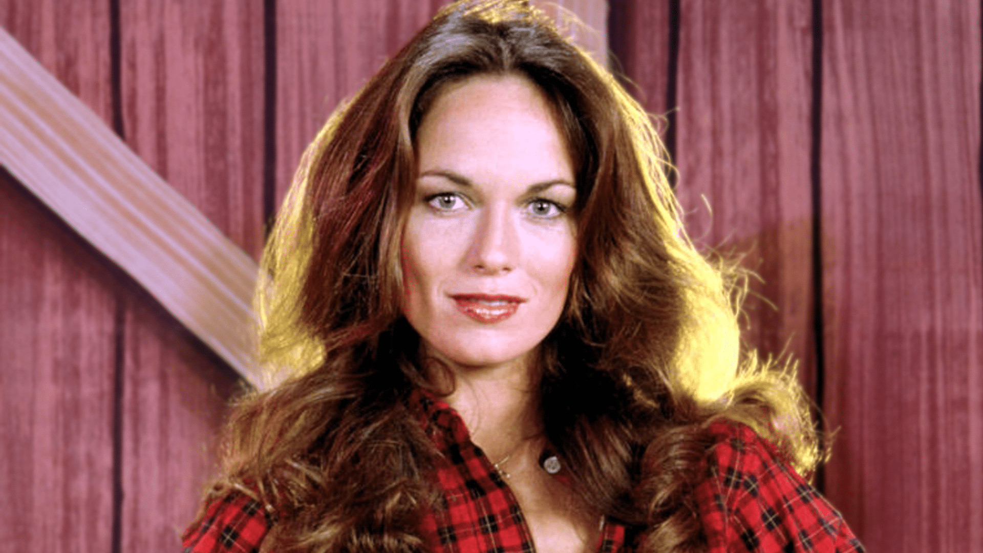 Actress Catherine Bach smiling in a vintage Dukes of Hazzard-era photo, as news emerges that she’s been hospitalized in Los Angeles following post-surgery complications.