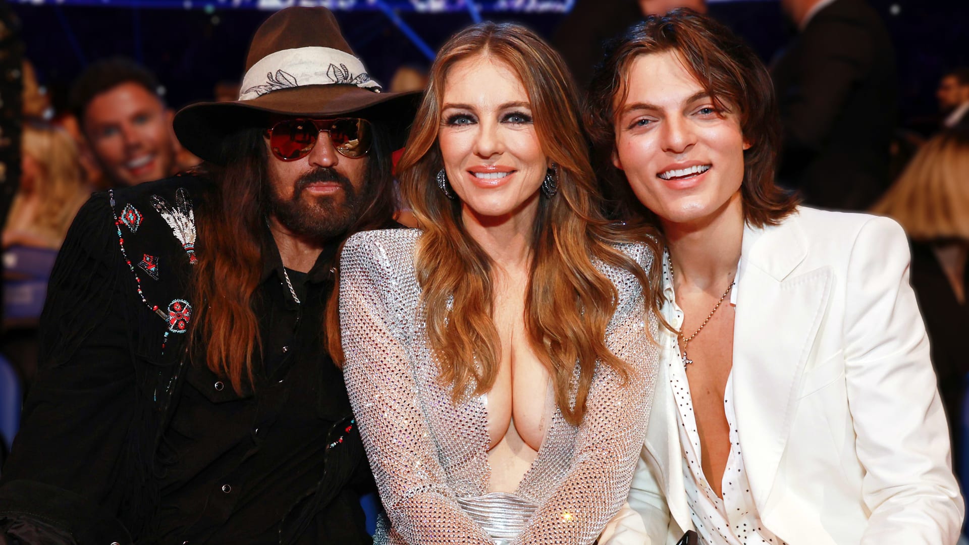 Billy Ray Cyrus left in cowboy hat and sunglasses next to Elizabeth Hurley center in sparkling silver gown and son Damian Hurley right in white suit jacket smiling together shutting down romance rumors 2025.
