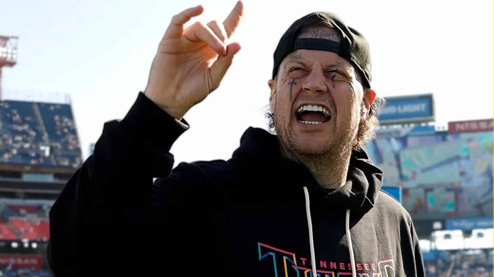 Jelly Roll goes viral with a rare clean-shaven selfie after massive 200-pound weight loss, throwing up the “hook ’em horns” hand sign while wearing a Tennessee Titans hoodie in a stadium.