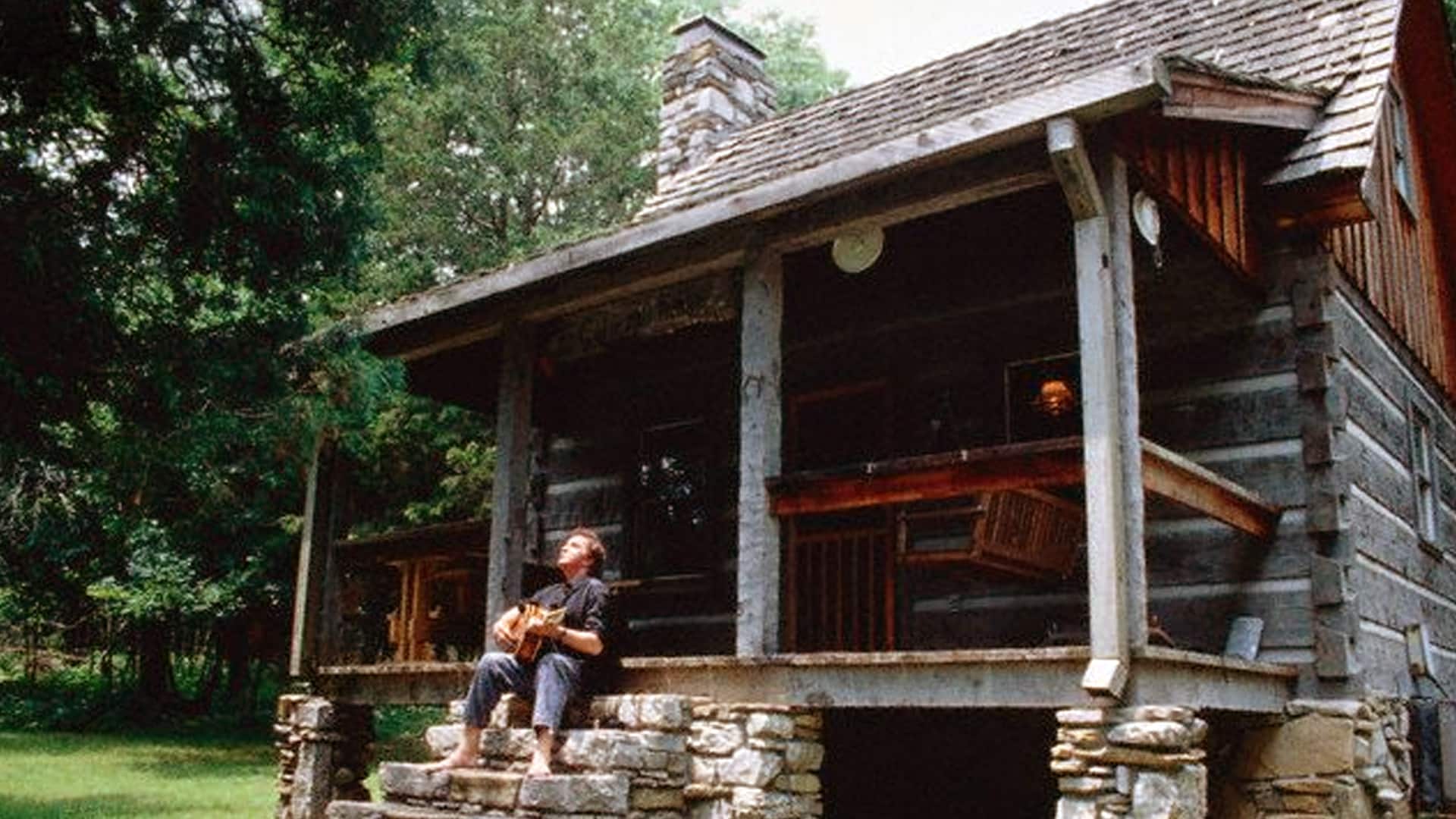 Johnny Cash relaxing with his guitar on the porch of the historic Cash Cabin in Hendersonville, the creative sanctuary he shared with June Carter.