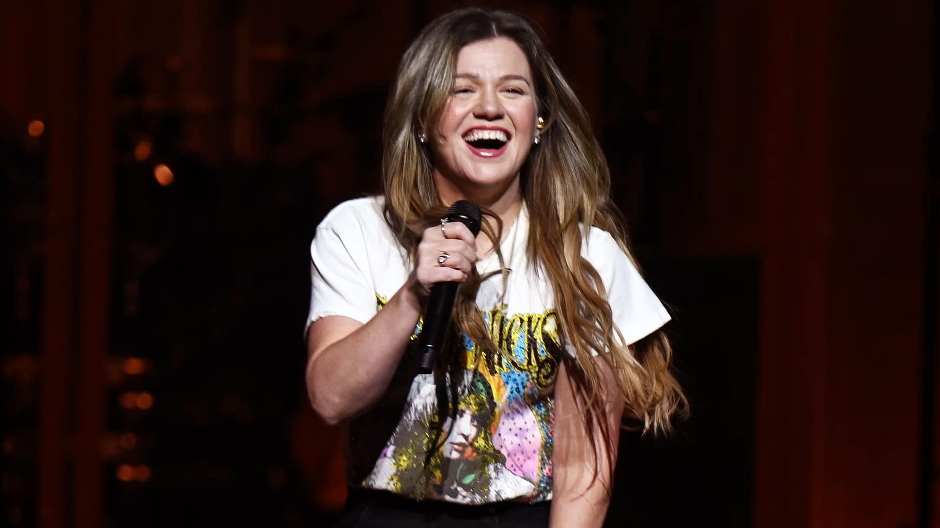 Kelly Clarkson smiling mid-performance, capturing the same loose, comic energy behind her playful jab at Blake Shelton during the Vegas vow renewal.