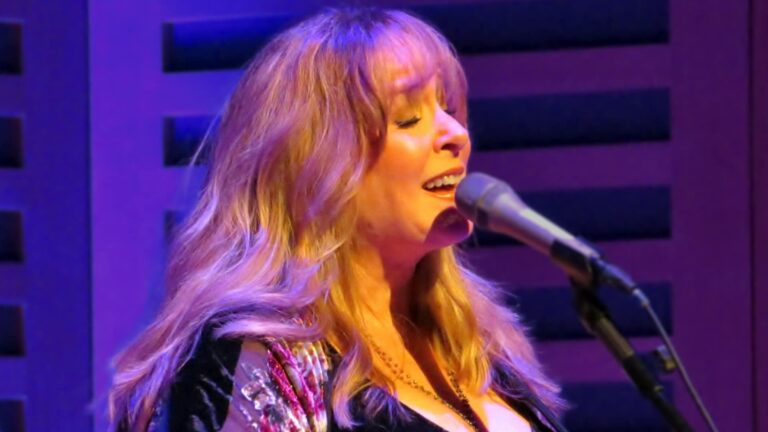 Gretchen Peters bathed in purple stage light, capturing the soulful presence behind the songwriting legacy that shaped hits for country greats.