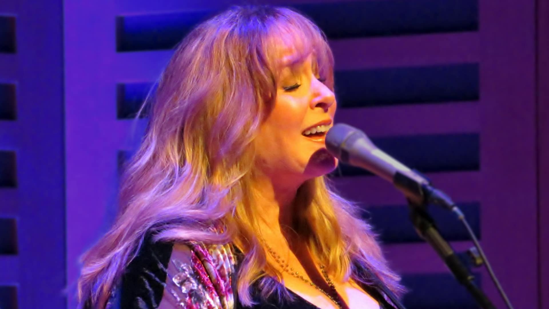 Gretchen Peters bathed in purple stage light, capturing the soulful presence behind the songwriting legacy that shaped hits for country greats.