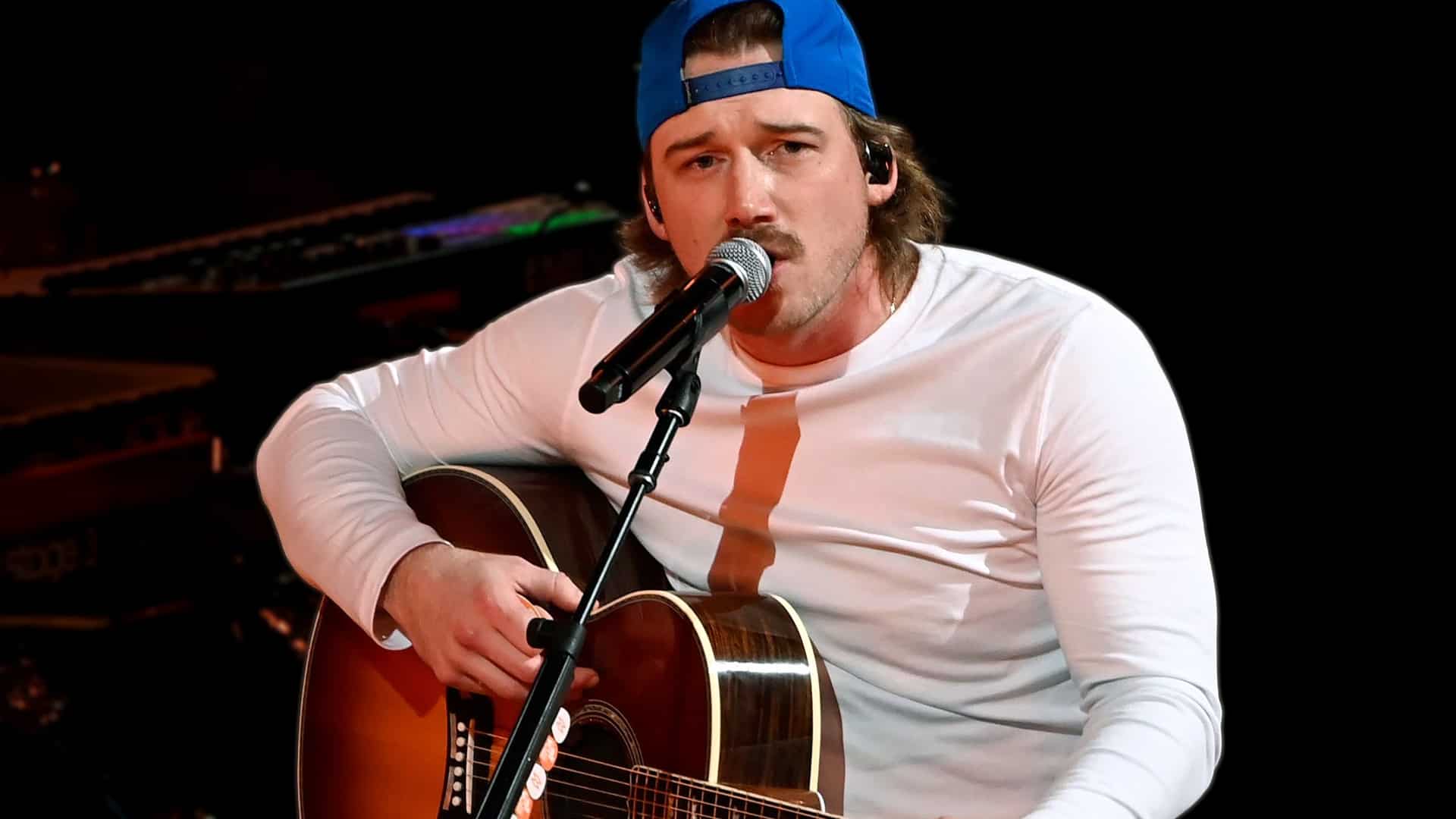 Morgan Wallen performing acoustic guitar on stage in white shirt and blue baseball cap celebrating three Spotify billion stream songs "Whiskey Glasses," "Last Night," and "I Had Some Help."