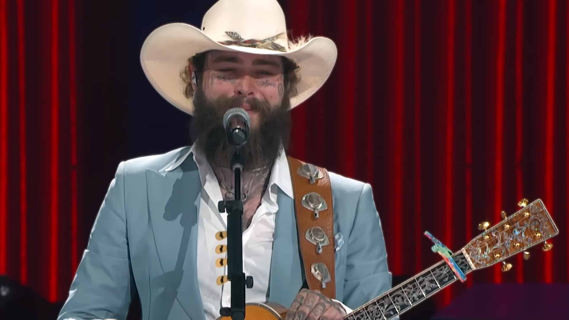 Close-up of Post Malone singing into microphone while strumming ornate guitar during live performance, highlighting his Nashville roots as he hosts complimentary Thanksgiving dinners for on-duty police, firefighters, and EMTs at Posty's Broadway location.