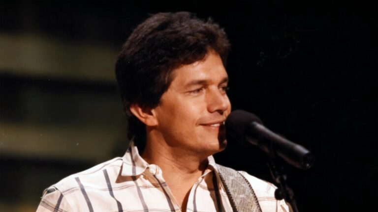 George Strait performing onstage in a plaid shirt, singing his first No. 1 hit “Fool Hearted Memory” alongside Texas fiddle legend Johnny Gimble.