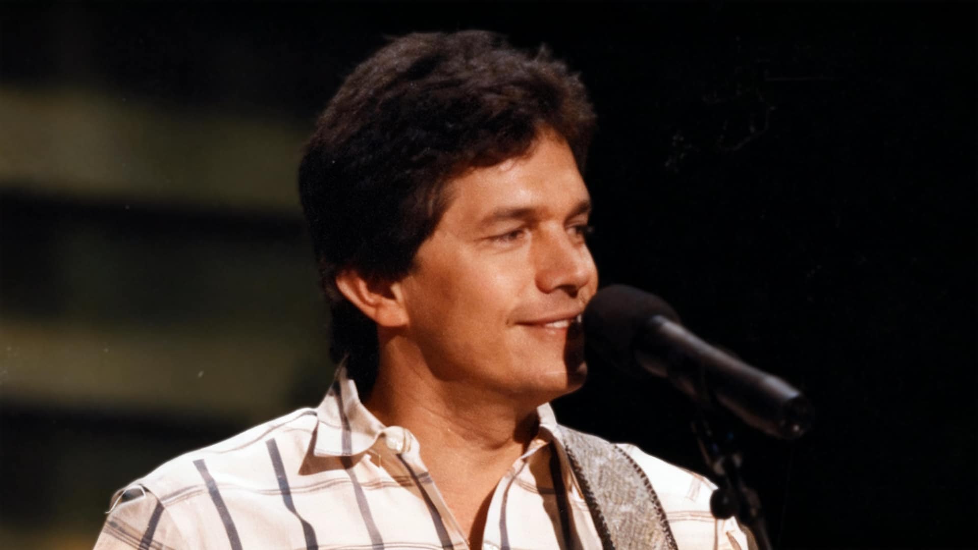 George Strait performing onstage in a plaid shirt, singing his first No. 1 hit “Fool Hearted Memory” alongside Texas fiddle legend Johnny Gimble.