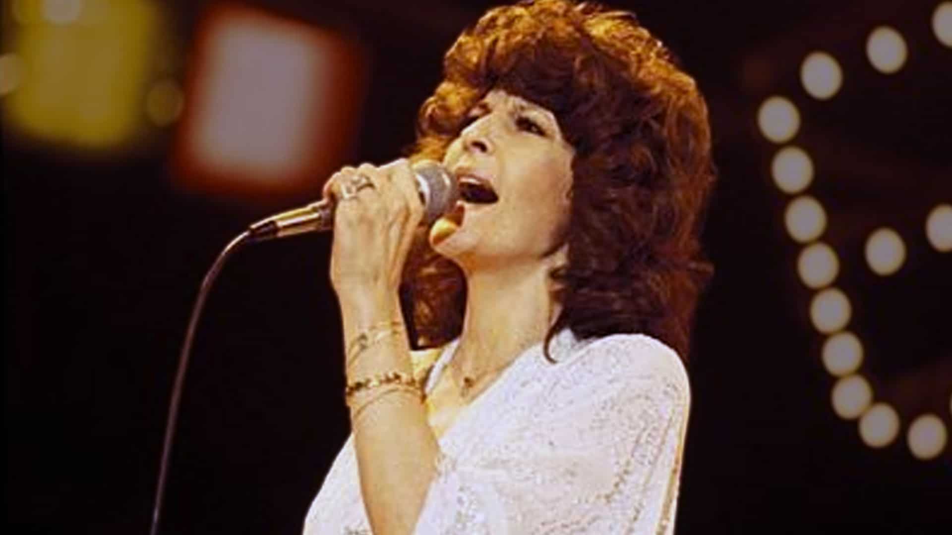 Donna Fargo performing onstage in a white outfit, the former high school teacher who became a Grammy-winning country star.