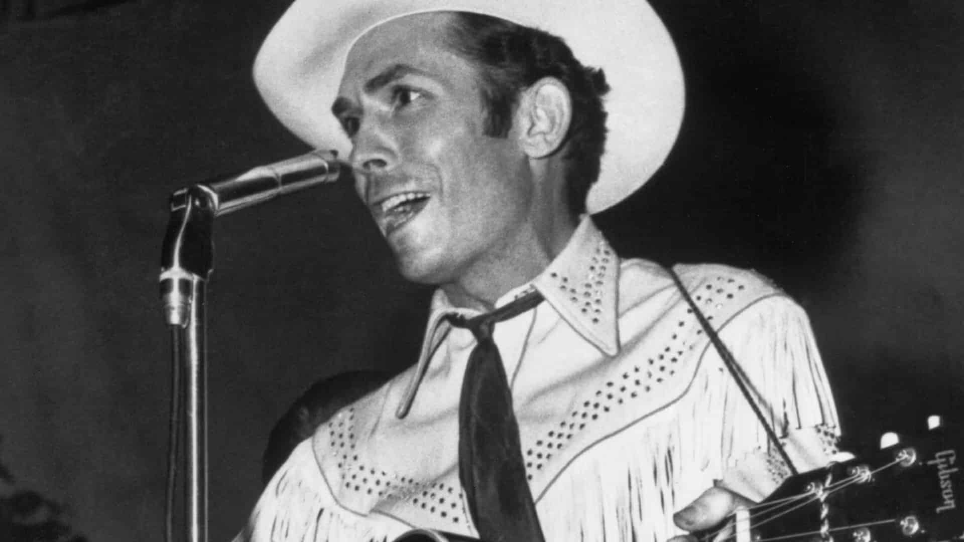 A young Hank Williams at the microphone in a fringed western shirt, catching the charge of the TV debut that helped carry his simple song to audiences across the country.