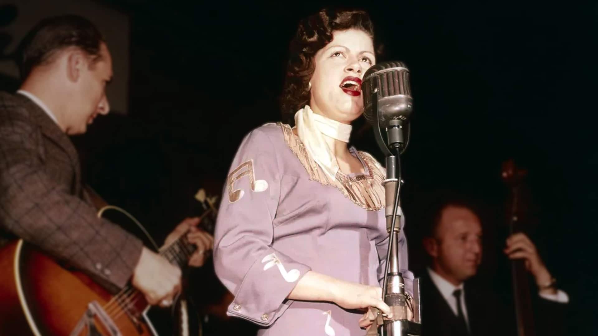 Patsy Cline in a music-note dress delivering a powerful lyric, capturing the spirit behind the recording session that sparked her first No. 1 hit.