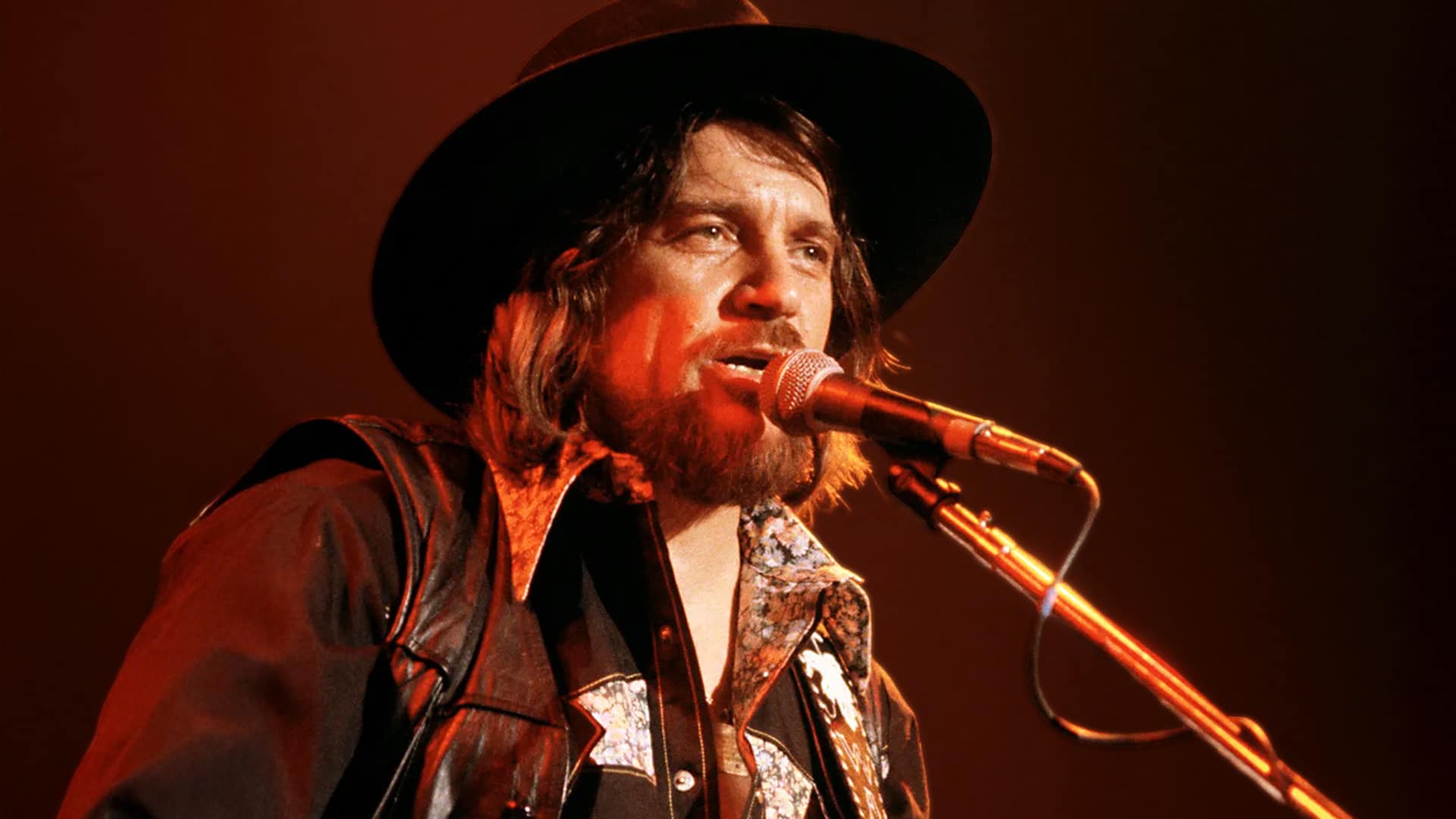 Waylon Jennings under red stage lights, capturing the fearless outlaw edge that fueled his unfiltered message on that 1975 CMA certificate.