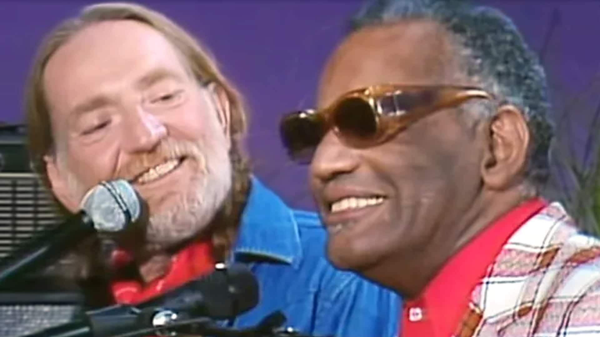 Willie Nelson and Ray Charles smiling together while performing, with Nelson at the microphone and Charles wearing sunglasses during a classic country duet moment.
