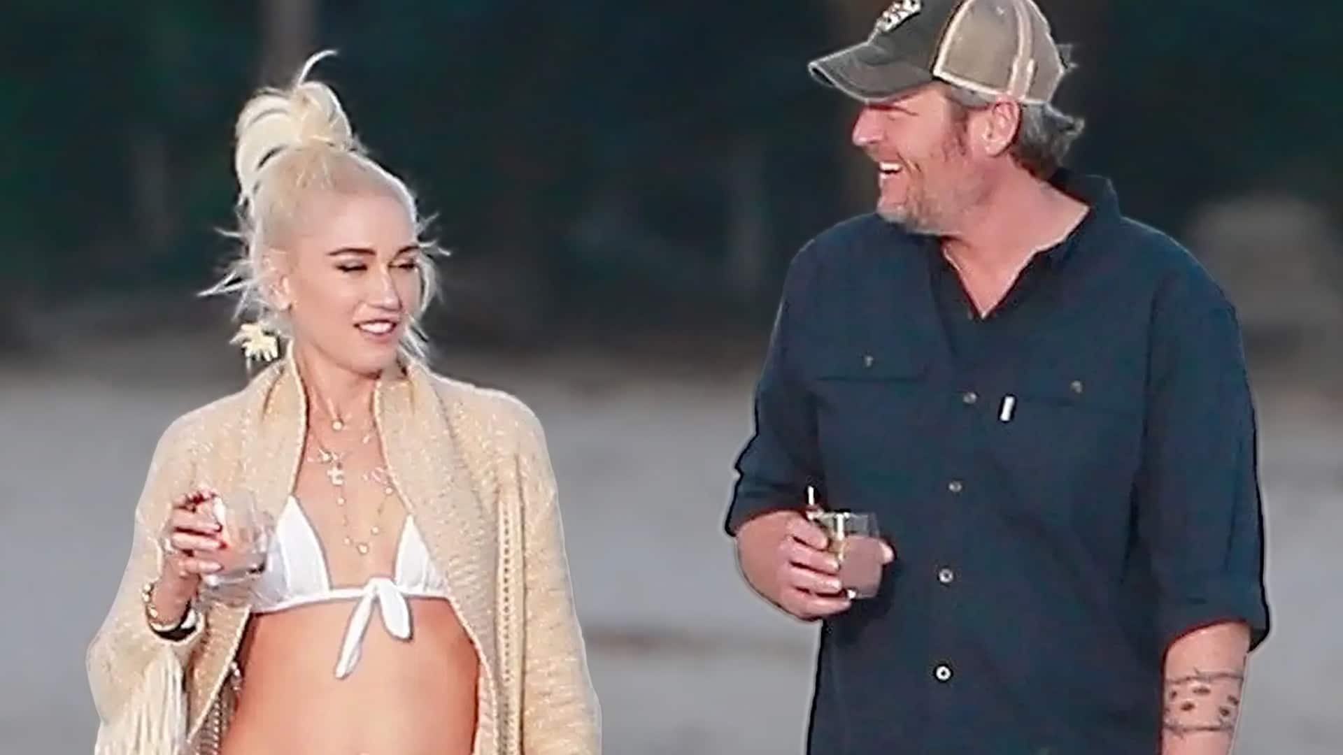 Blake Shelton and Gwen Stefani walking together amid marriage strain rumors, Gwen in a white bikini top and beige cardigan with high ponytail, Blake in a dark shirt and baseball cap holding a drink, highlighting the growing tension between their country and Hollywood lifestyles.