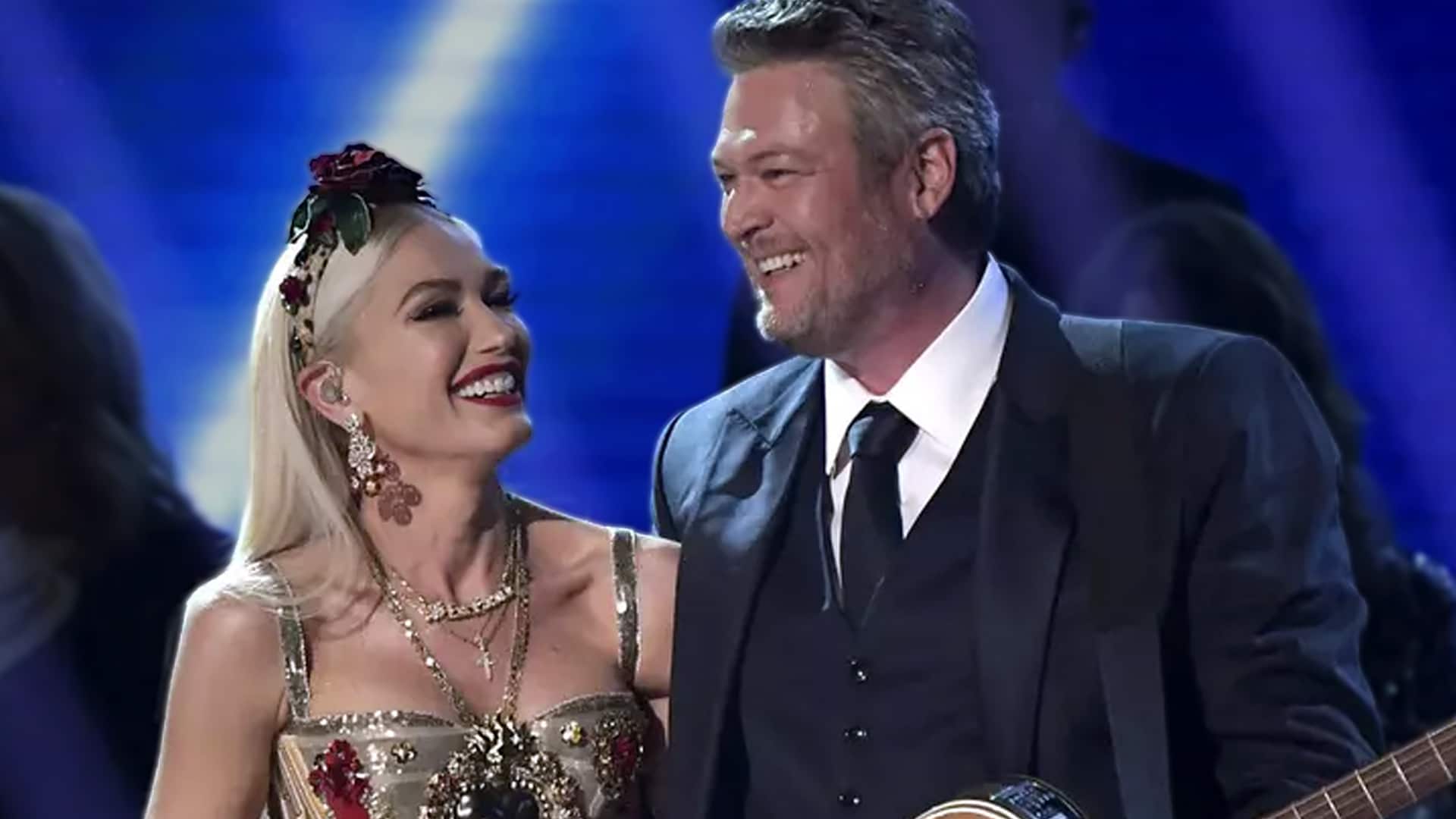 Blake Shelton and Gwen Stefani share a joyful moment on stage, Gwen in a sparkling floral gown with red rose headpiece and Blake in a dark suit holding a guitar, proving their romantic chemistry and marriage spark remain strong in 2025 despite breakup rumors.