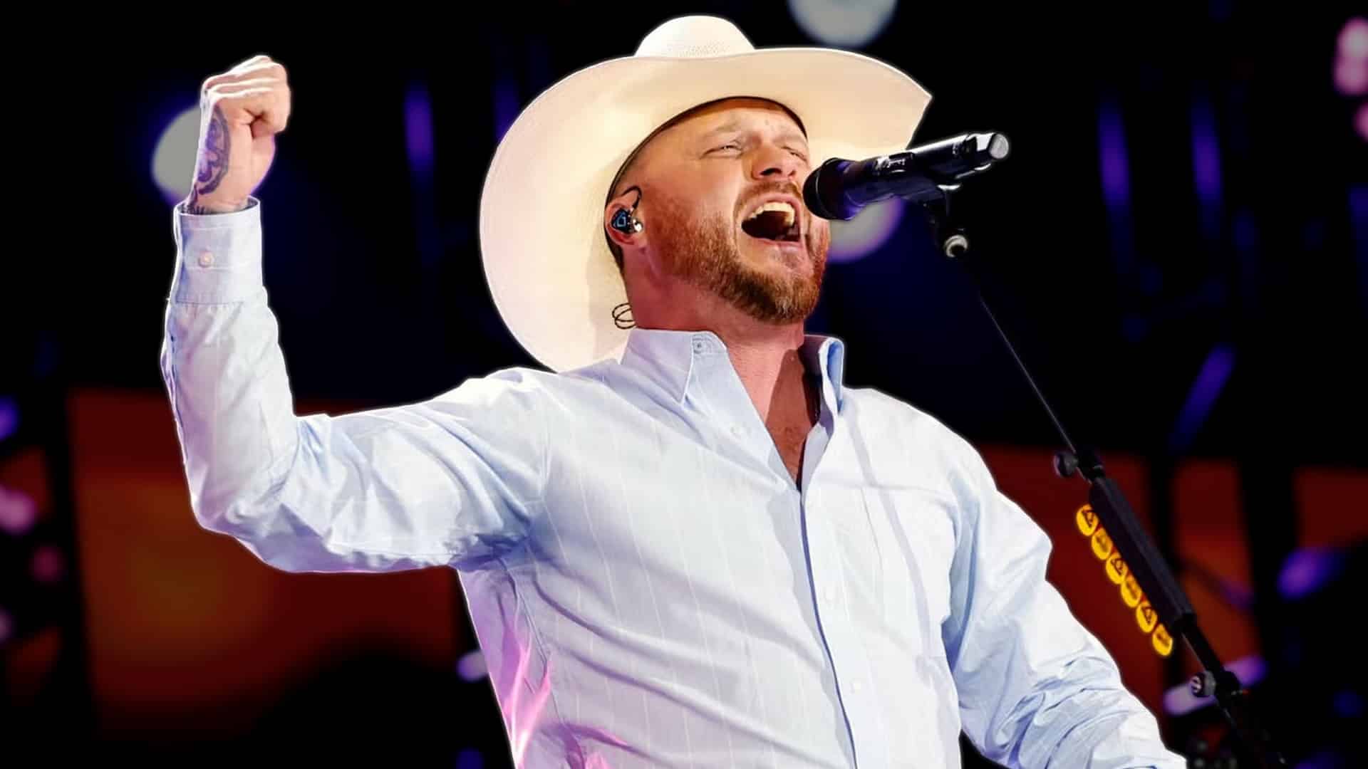 Cody Johnson performs passionately on stage in white cowboy hat and light shirt, raising his fist while singing, recalling the broke Christmas when he gave away his last $20 only to receive a miracle check in the mail shortly after marriage.