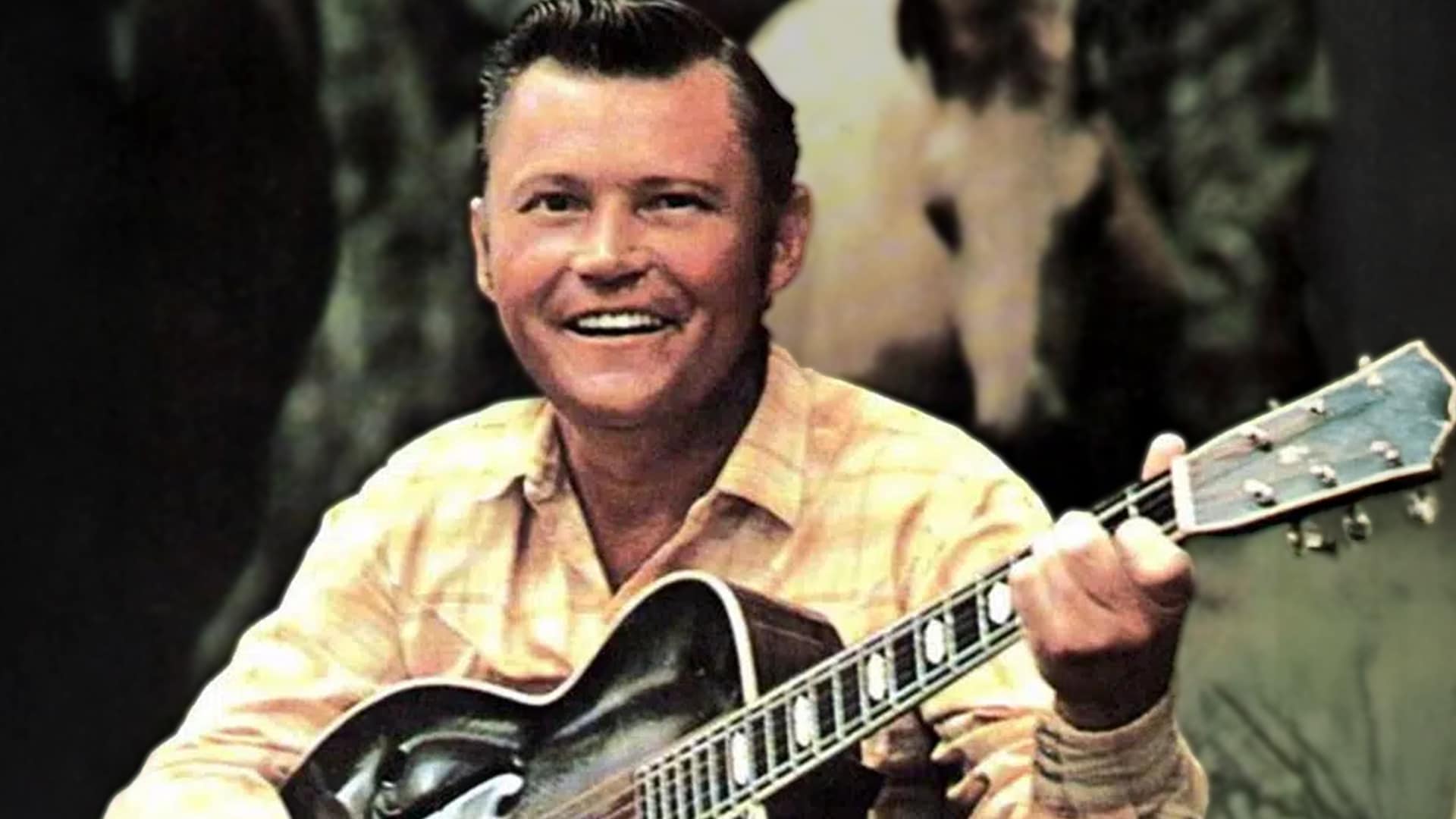 Country music legend Stonewall Jackson smiling with his signature black Gretsch guitar in a vintage 1950s photo, remembered four years after his 2021 death as the only artist ever invited to join the Grand Ole Opry before signing a record deal in 1956.