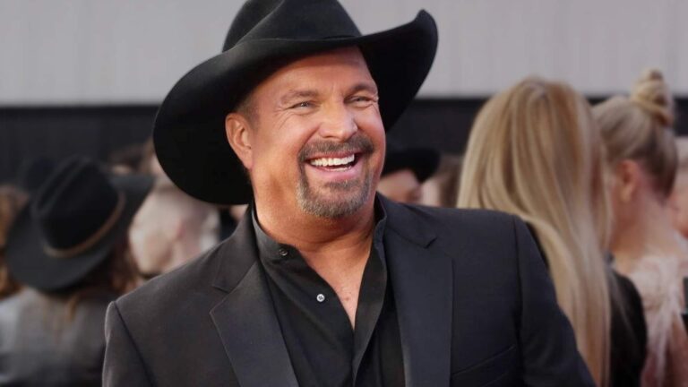 Garth Brooks smiling on the red carpet in black cowboy hat and suit jacket, famous for his hilarious Christmas prank of gifting two cans of beets in a Beats headphone box during a family "Silly Santa" exchange with wife Trisha Yearwood.