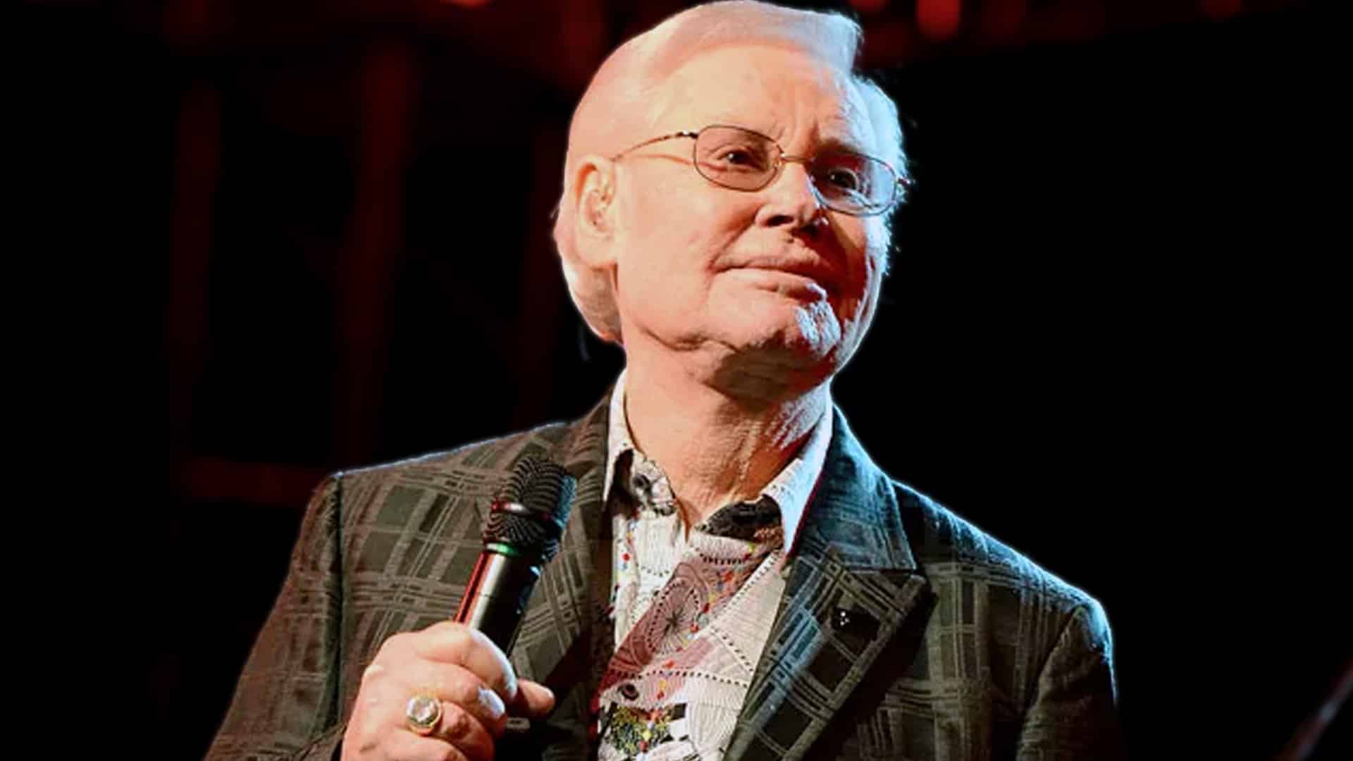 Classic photo of country legend George Jones performing with microphone in plaid jacket and patterned tie, as his booking agent reveals the telltale sign of drunken "No Show Jones" nights was hair not stiffened with hairspray in wild stories from his chaotic era.