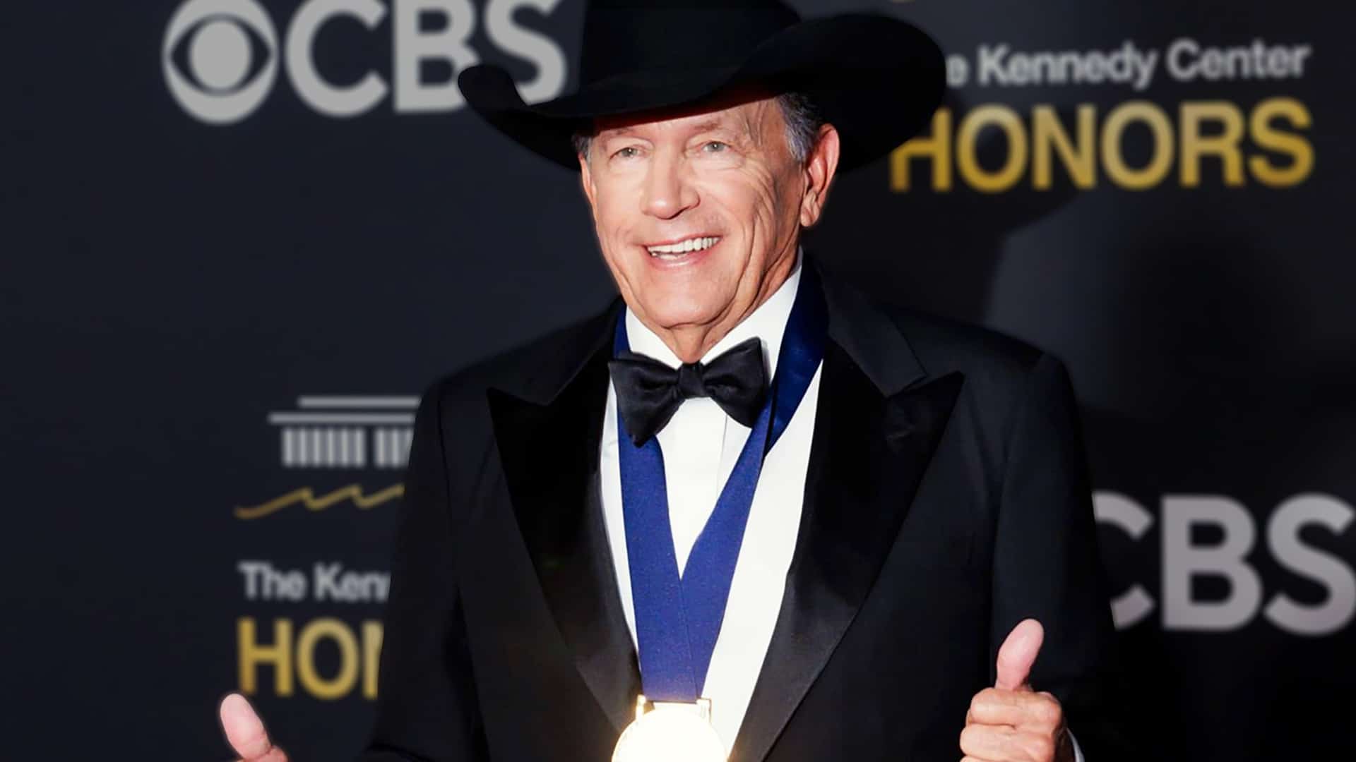 George Strait smiles with thumbs up in black cowboy hat and tuxedo wearing his Kennedy Center Honors medal at the 2025 ceremony, receiving emotional tributes from Miranda Lambert, Brooks & Dunn, and Vince Gill celebrating his legendary country career.